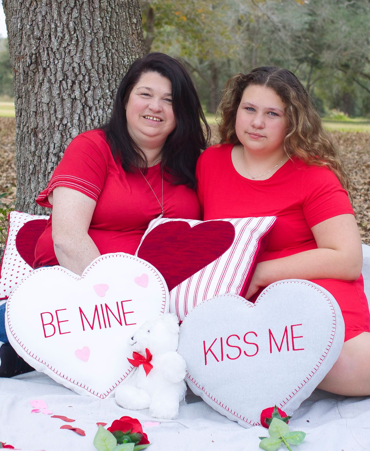 Valentine's themed outdoor photo with two people in red tops posing with decorative heart pillows.