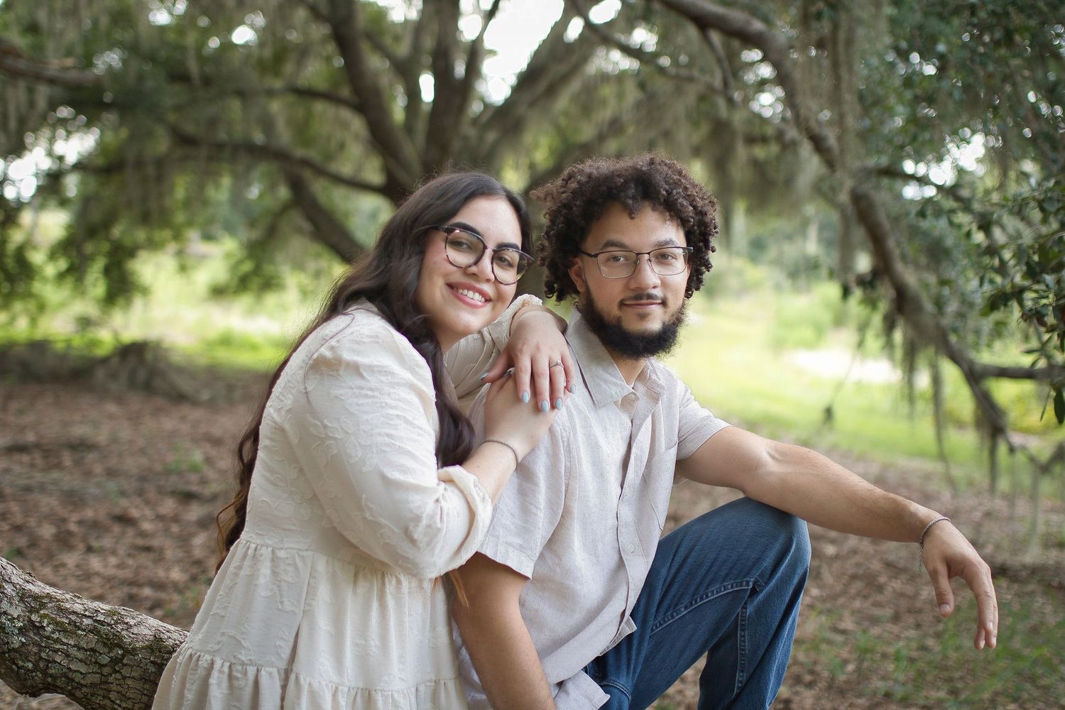 A couple shares tender moments in a park setting wearing matching white outfits while embracing and enjoying time together.