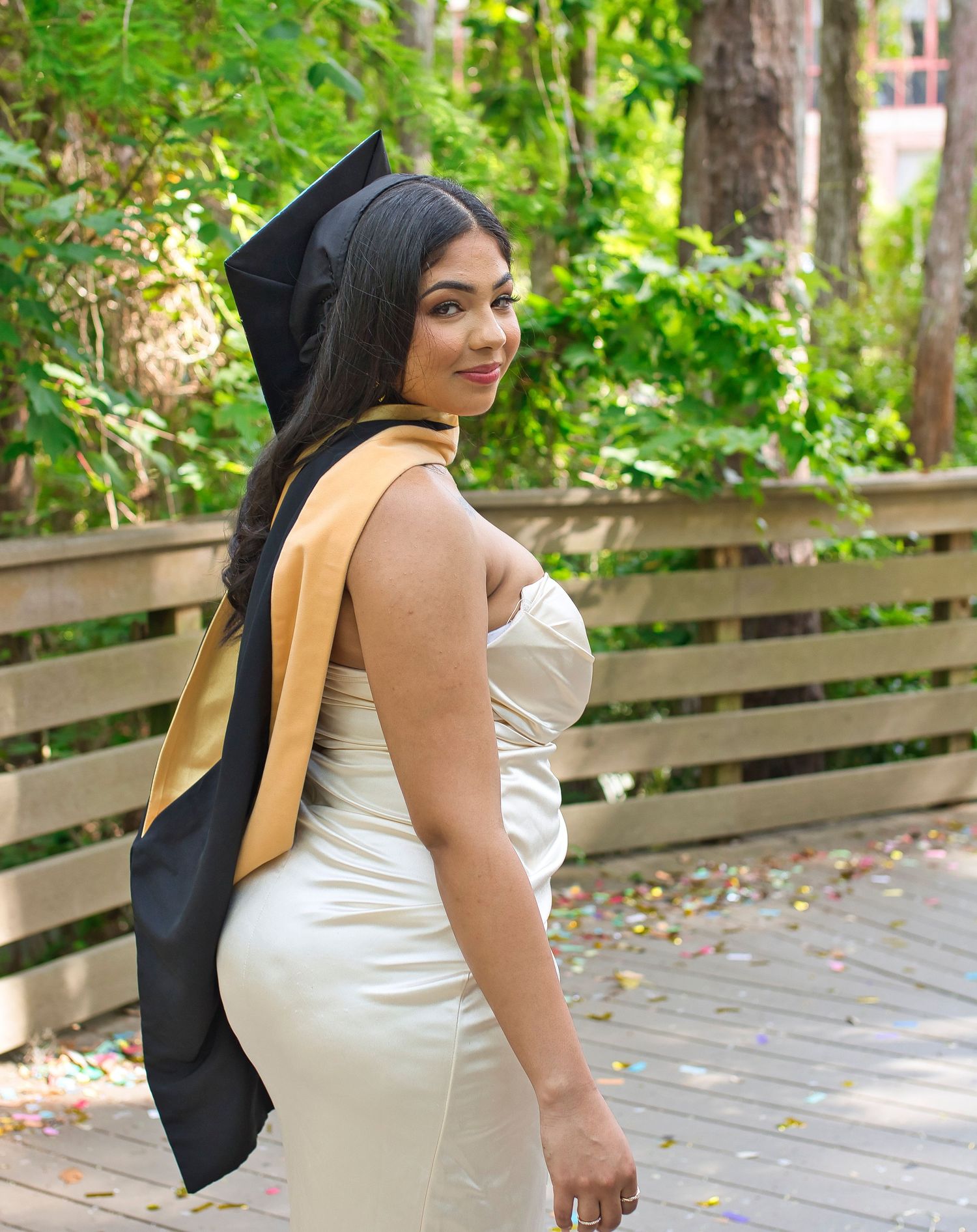A woman carries a tan backpack while walking along a wooden boardwalk path surrounded by lush green foliage.
