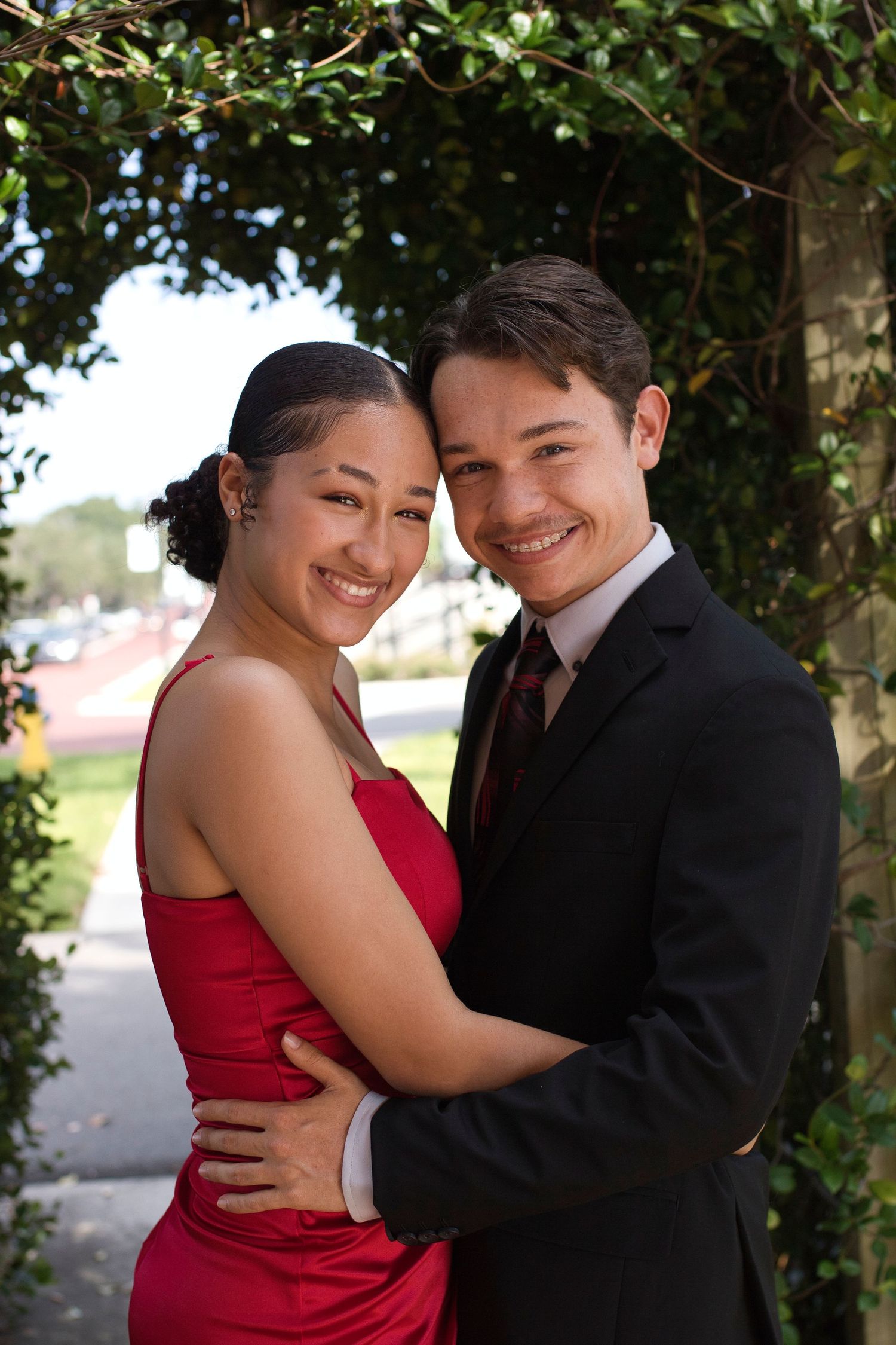 A couple in formal attire share a romantic moment under greenery.