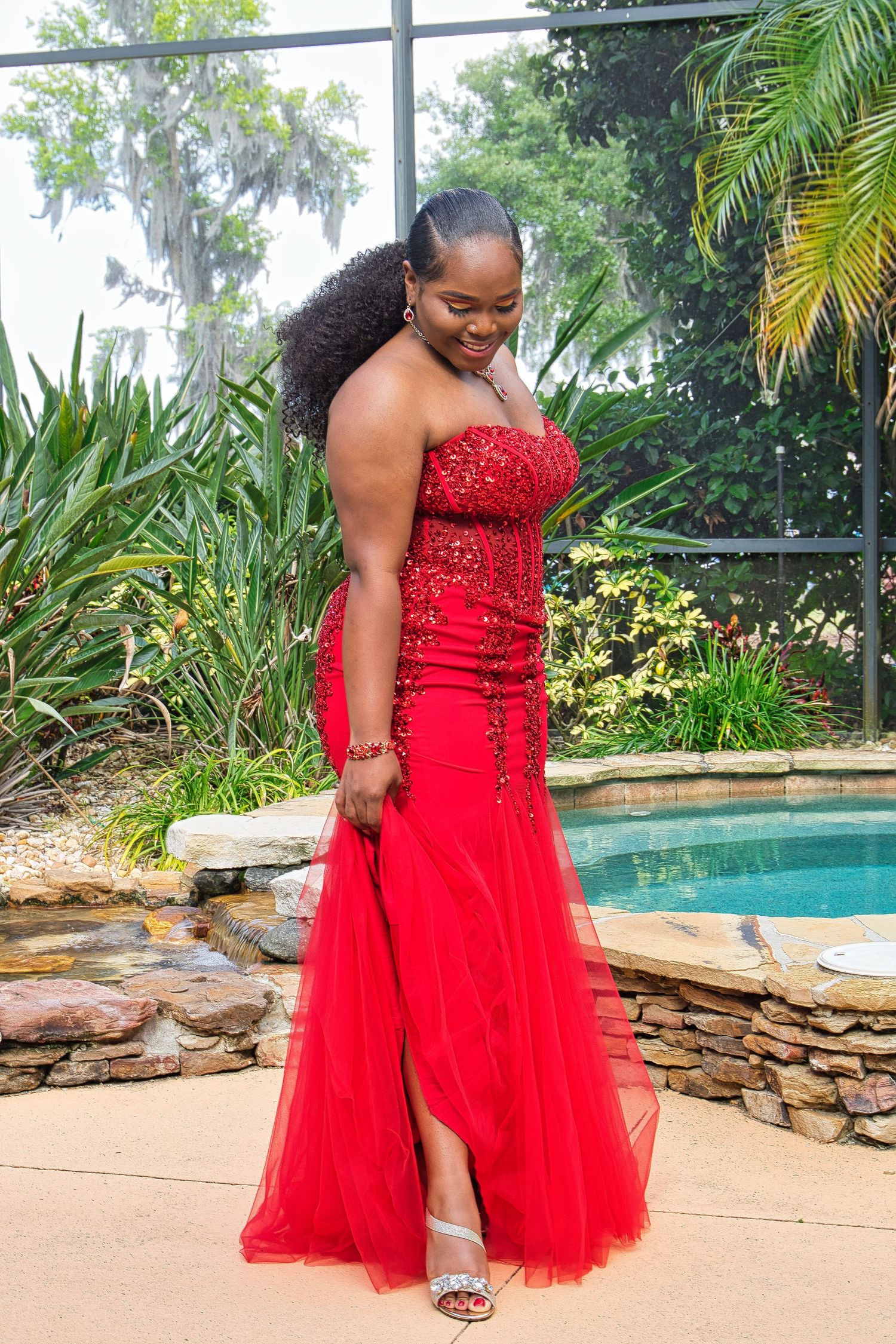 Stunning red formal dress with tulle skirt and beaded bodice shown in an outdoor setting.