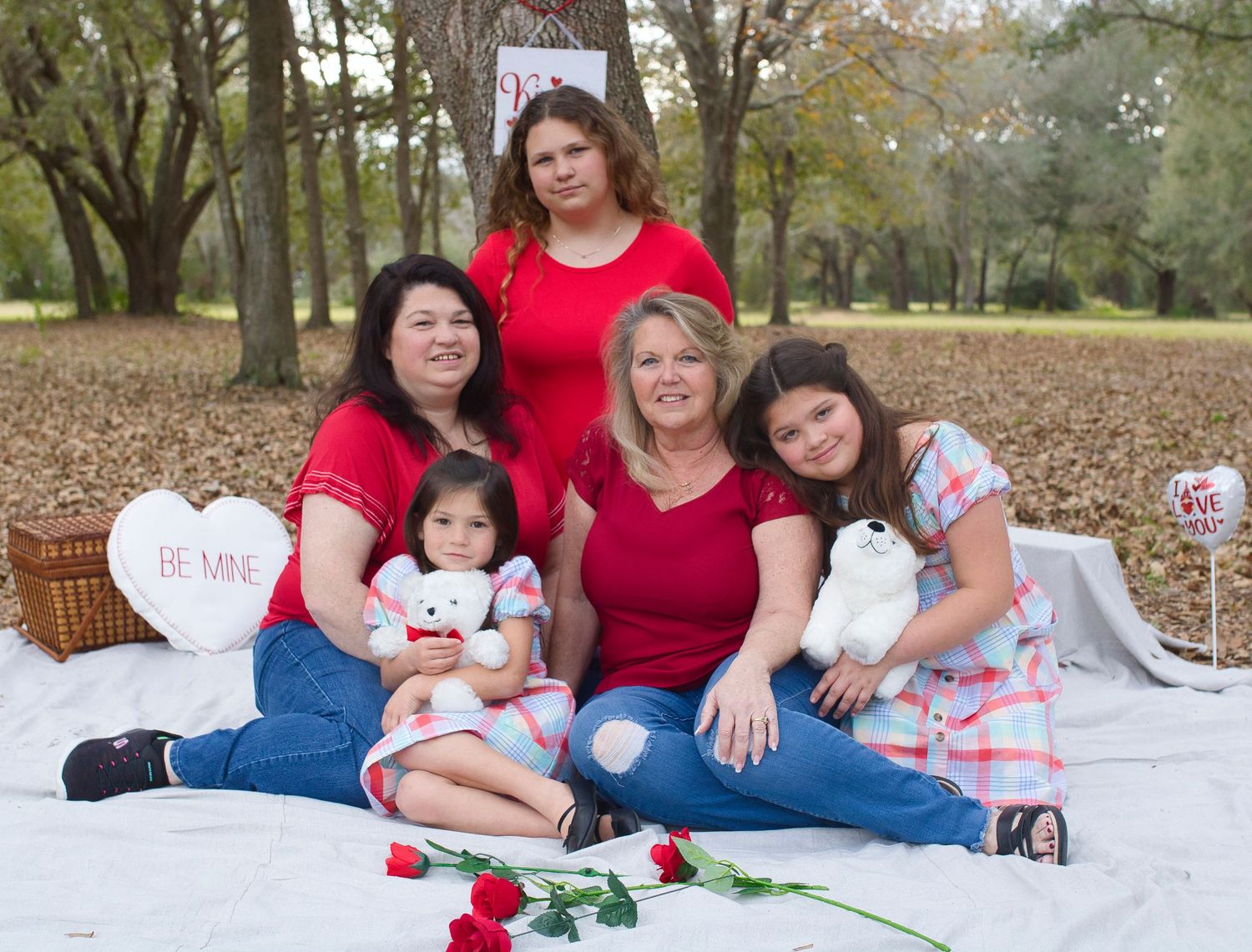 A group in matching red shirts having a picnic on a white blanket with roses and Valentine's hearts.