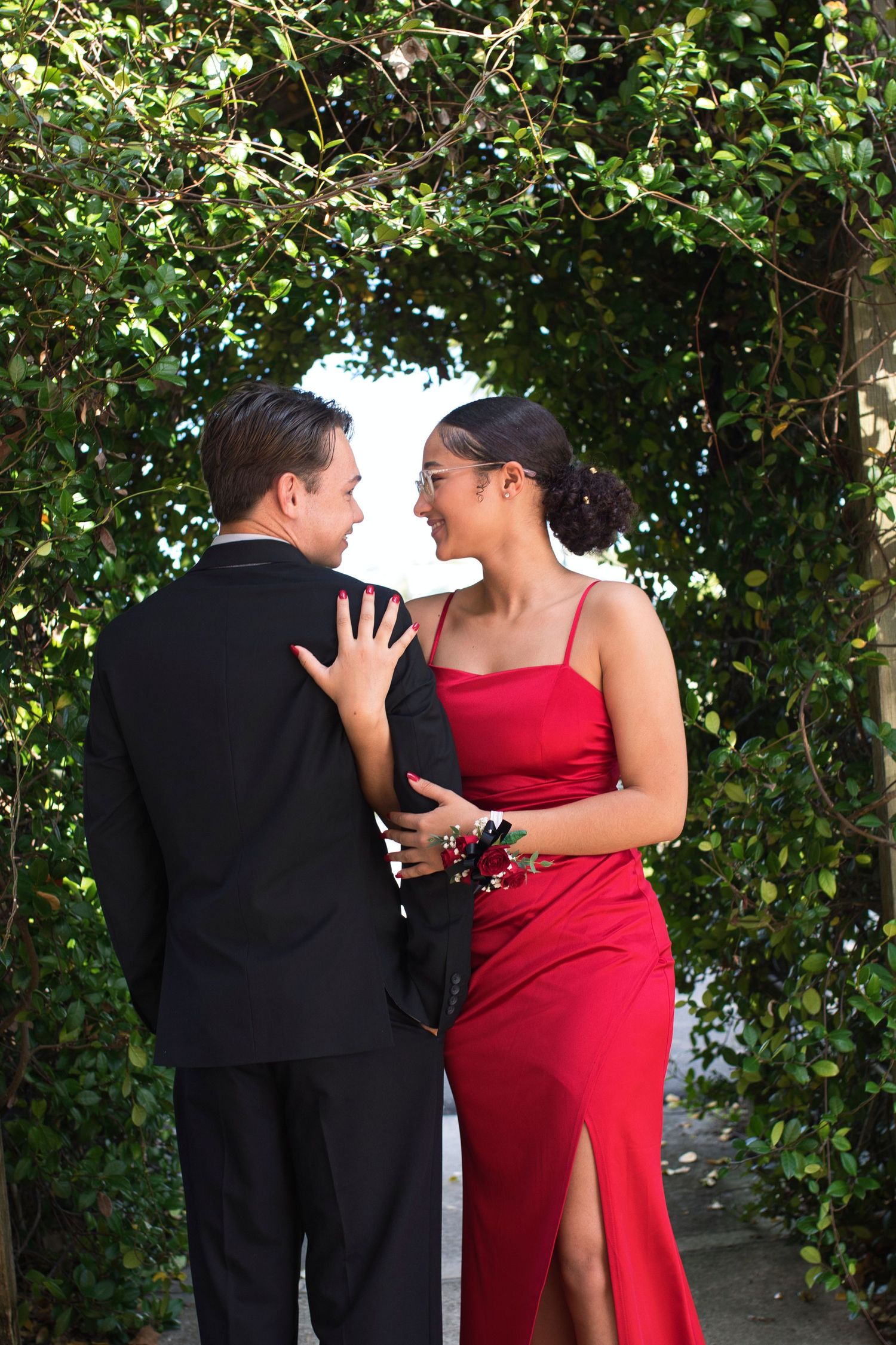 Couple in formal attire sharing intimate moment under leafy archway.