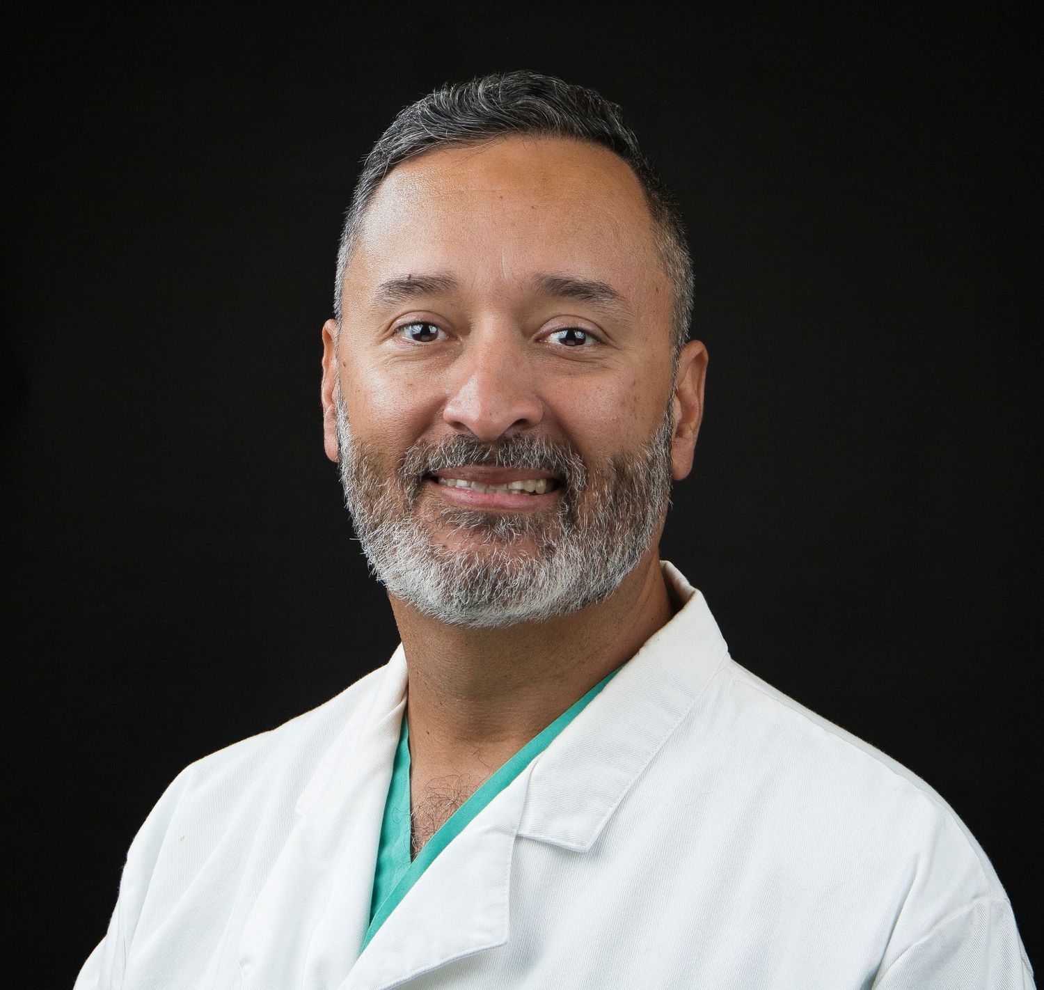 Healthcare provider wearing white coat and green scrubs poses for professional portrait.