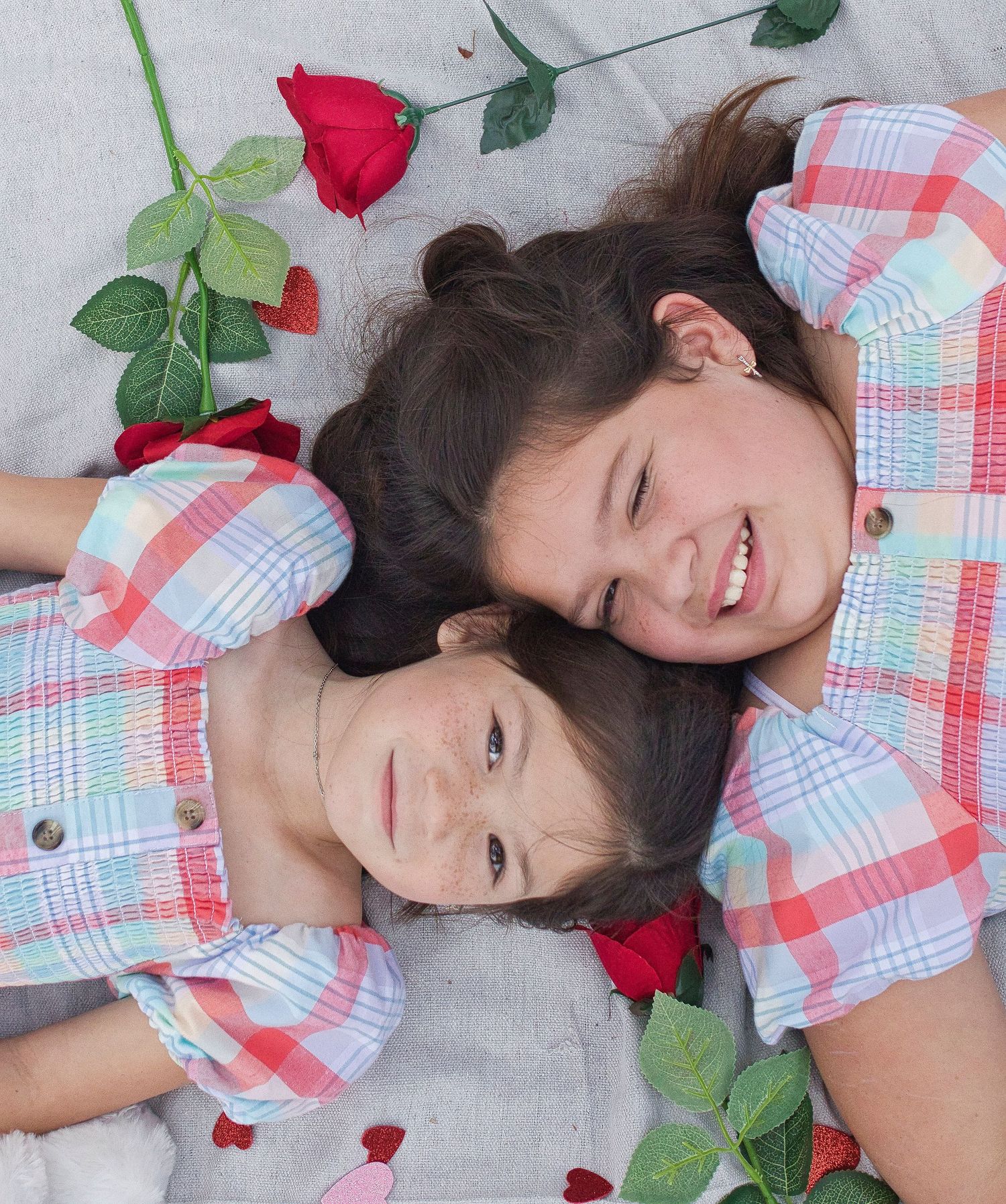 Valentine's themed portrait of two in matching plaid outfits laying with roses on white backdrop.