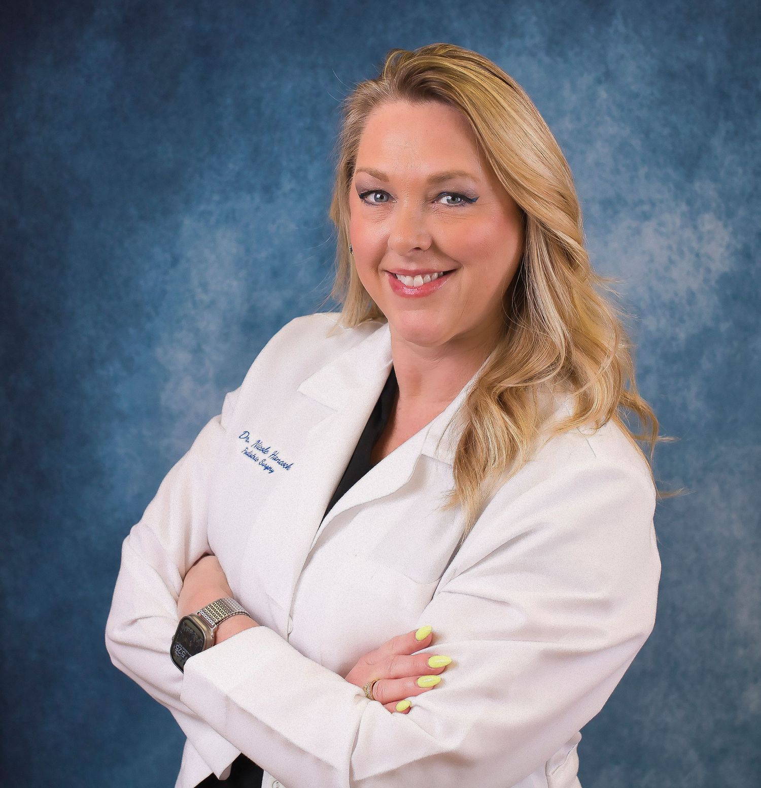 Smiling female doctor in white lab coat with arms crossed against blue background.