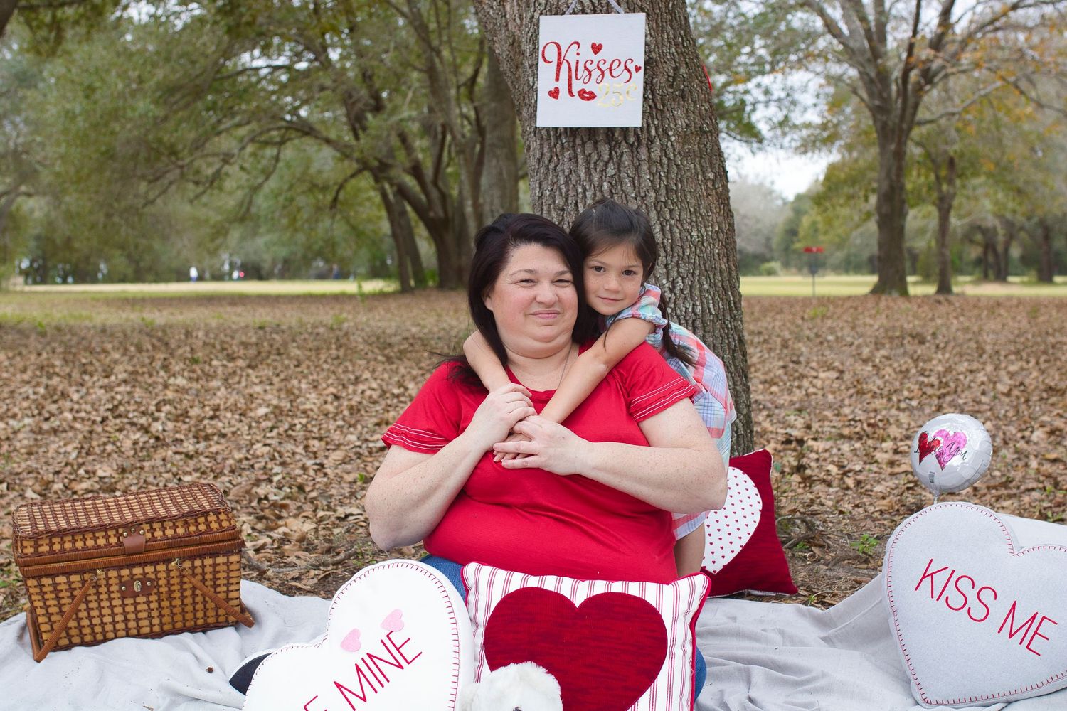 Casual family Valentine's photo shoot under tree with heart pillows and picnic basket.