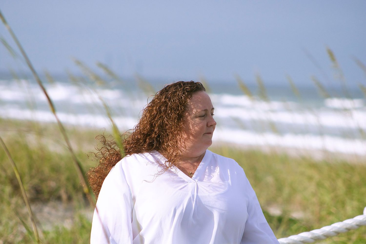 Beach scene with person in white shirt standing near coastal dunes.