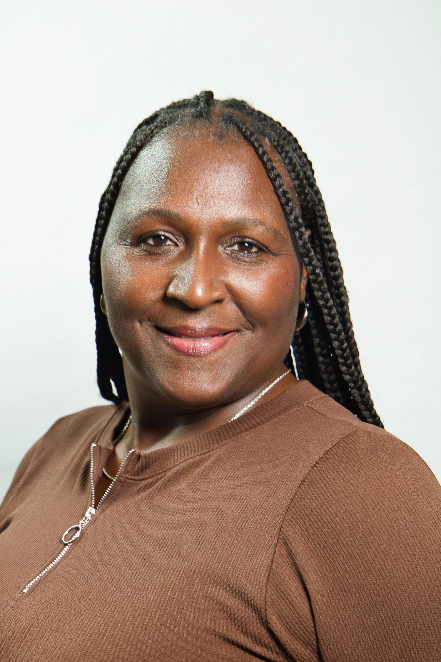 Smiling Black woman with braided hair wearing a brown turtleneck and silver necklace against a light background.