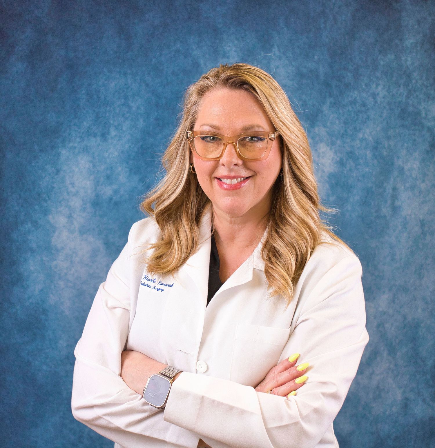 Smiling female healthcare professional in white lab coat with arms crossed against blue background.