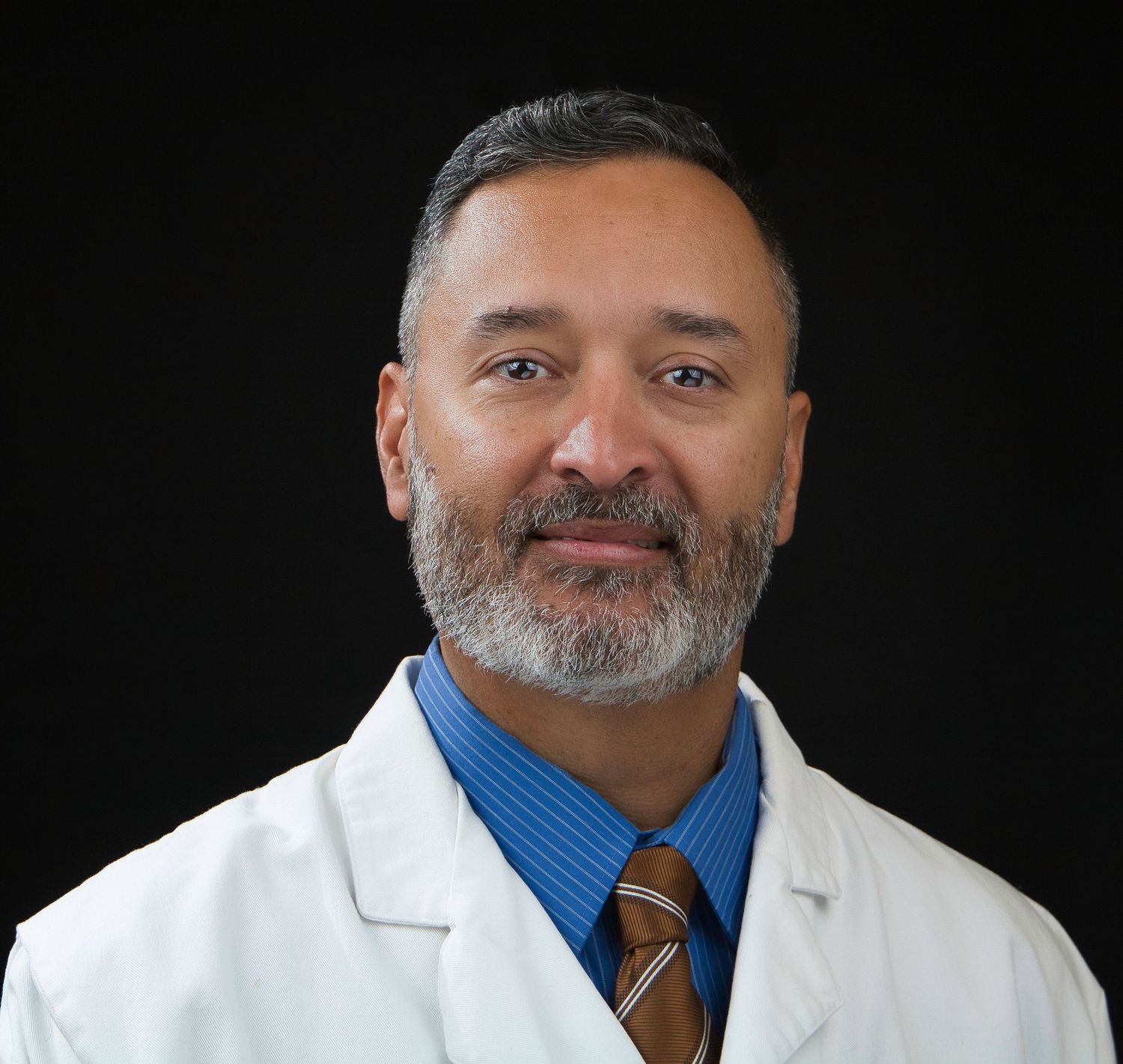 Medical professional in white coat and blue shirt with tie poses for professional headshot.