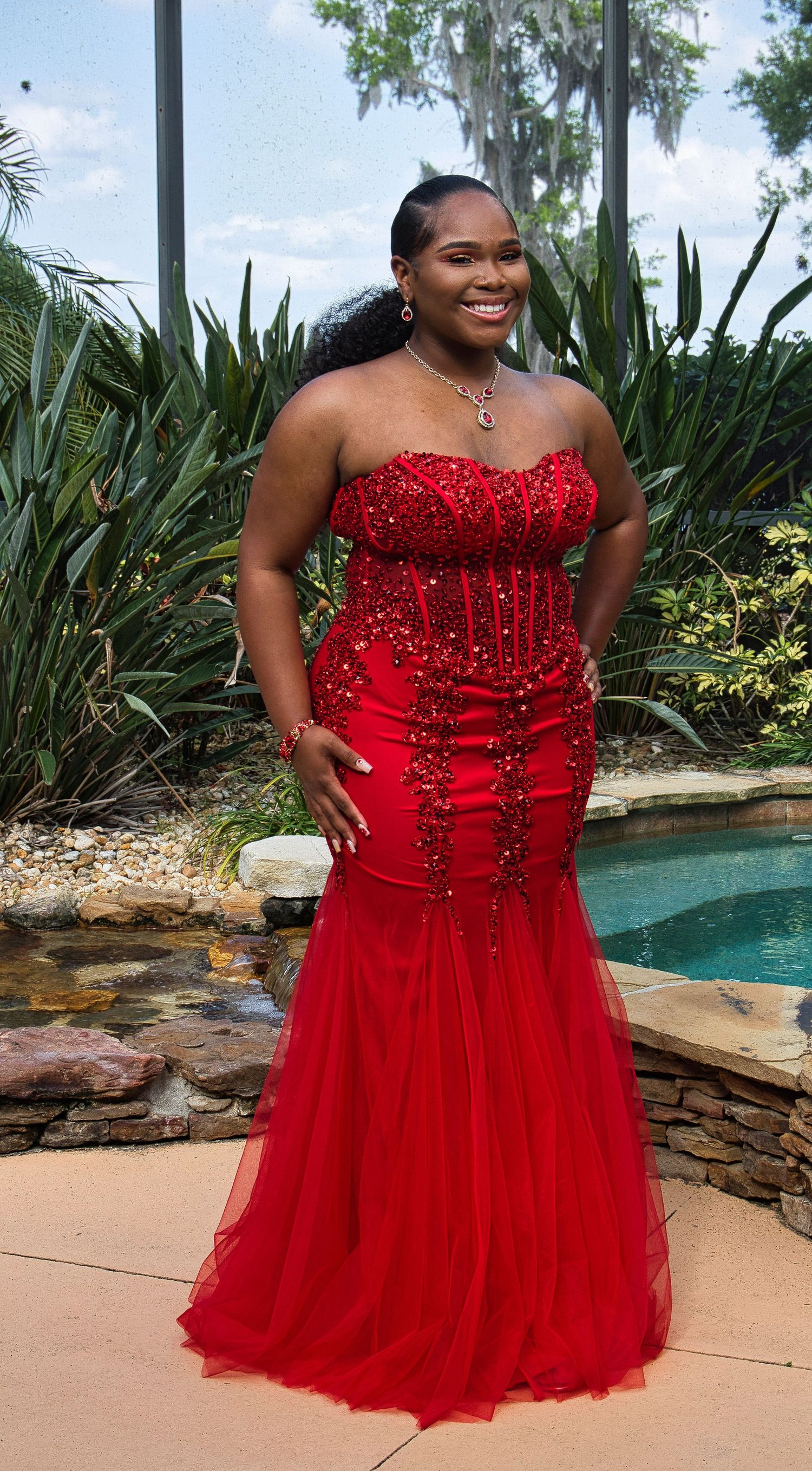 A stunning red mermaid-style formal gown with beaded embellishments photographed by a pool.