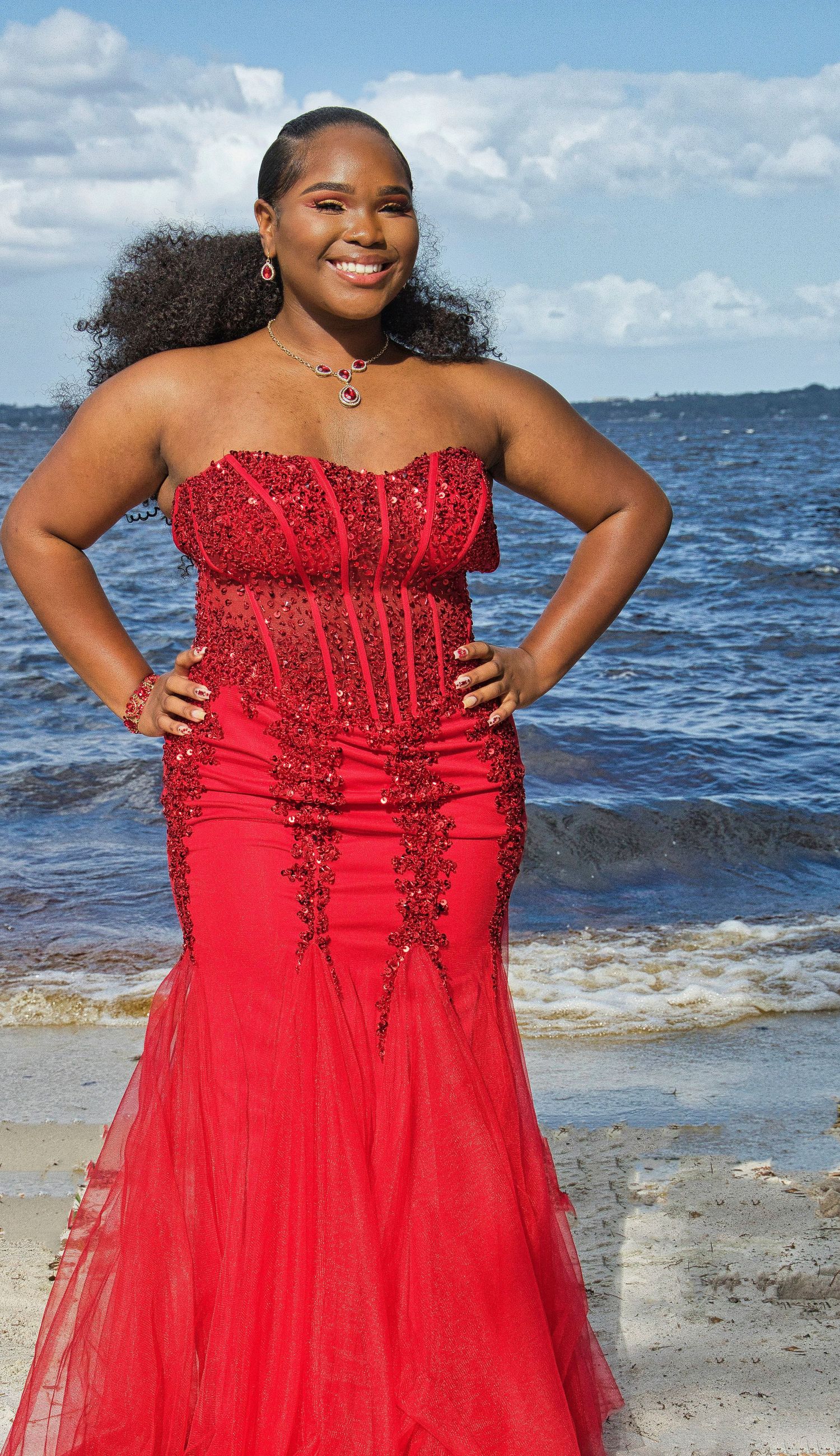 Beaded red formal gown with mermaid silhouette photographed against an ocean backdrop.
