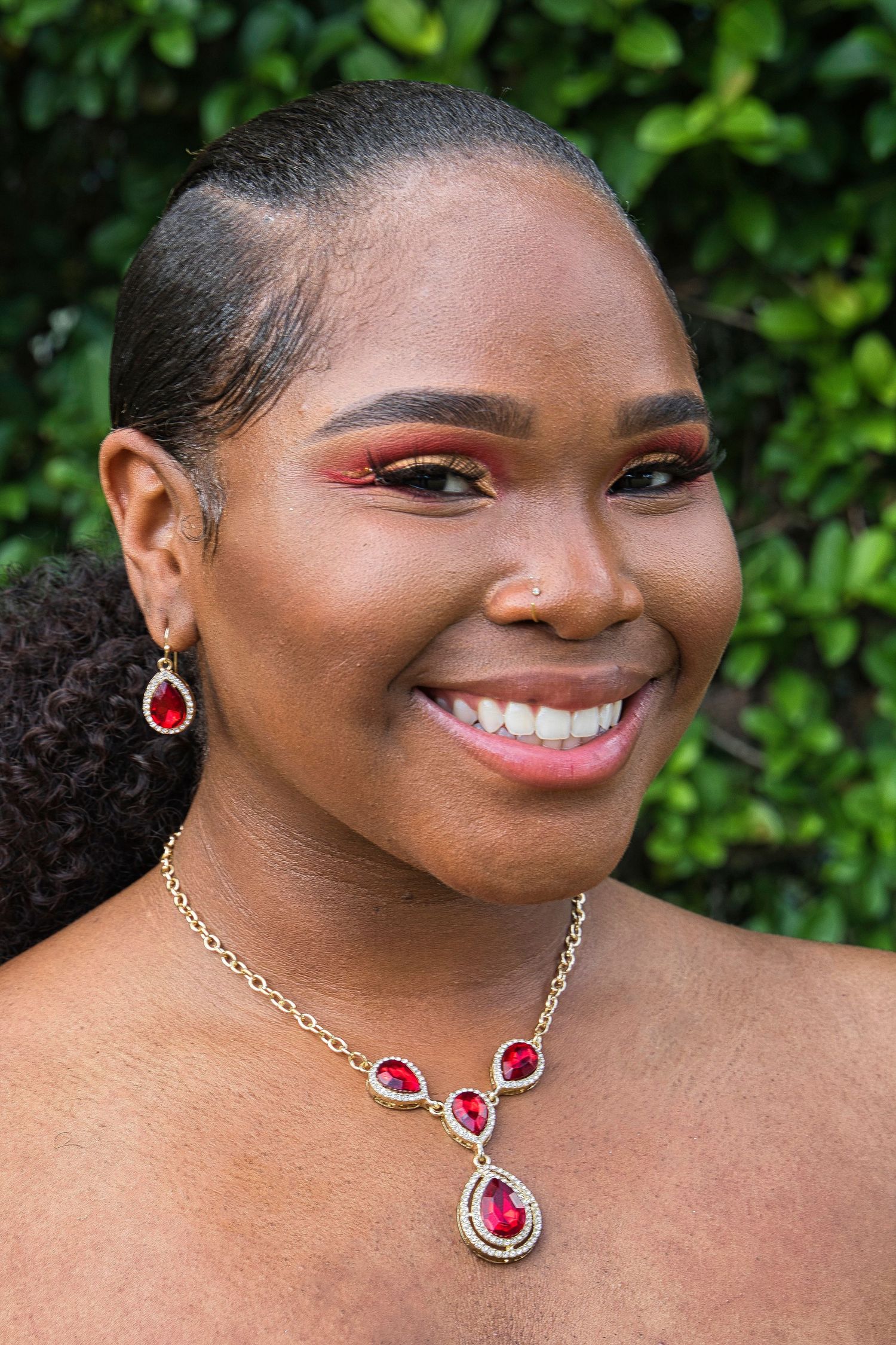 Ruby red jewelry set with matching earrings and necklace against natural greenery.