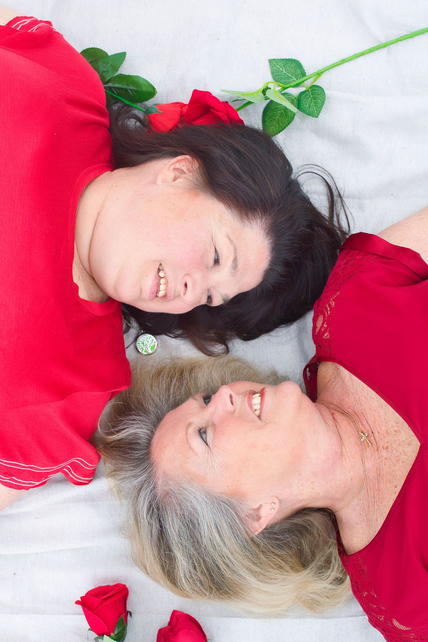 Overhead portrait with red roses showing two people in red tops laying on white background.
