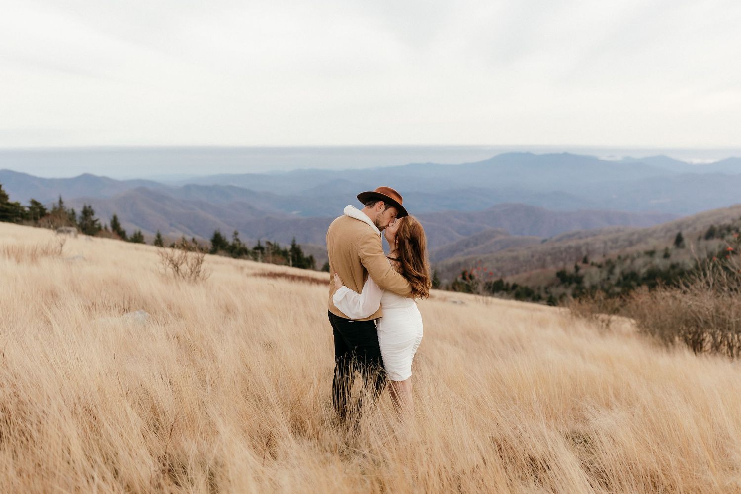 couple shares a kiss on top of a mountain as they gaze upon the beautiful mountain rows of north carolina