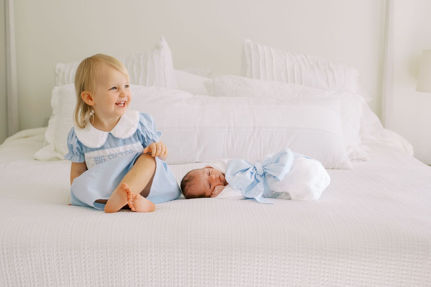 A series of soft, dreamy photos showing a newborn baby and sibling in white bedding with natural lighting.