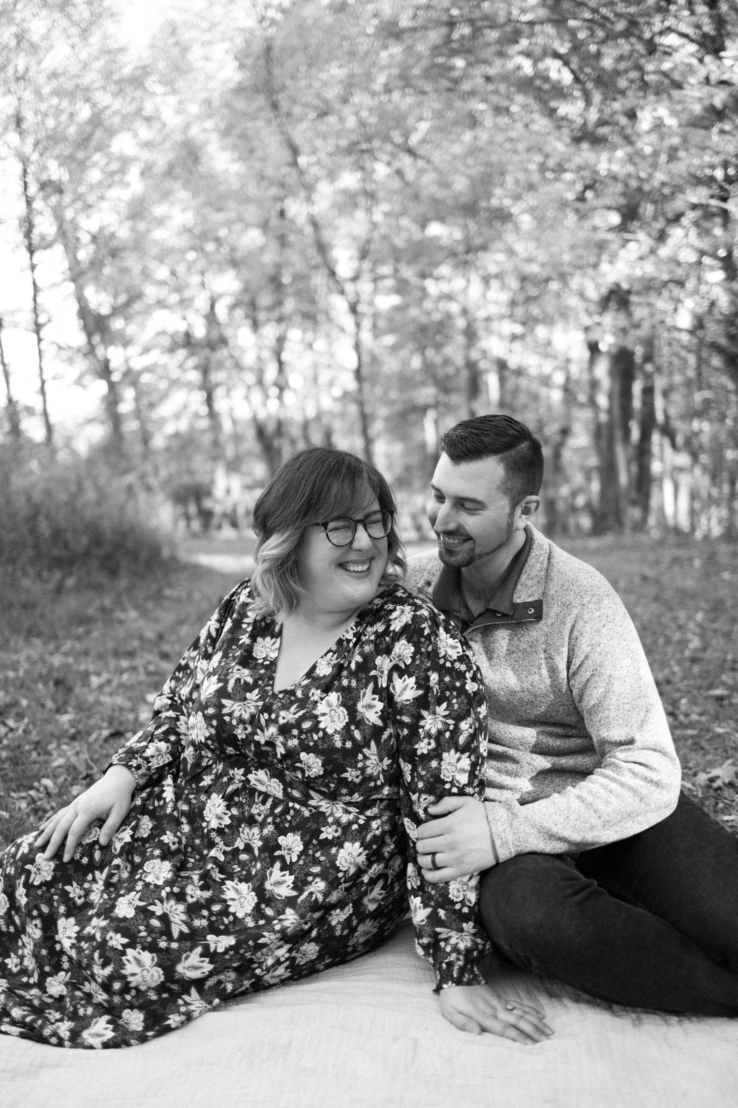 A couple shares an intimate moment while sitting on a blanket in a wooded area, captured in black and white photography in hunterdon county.