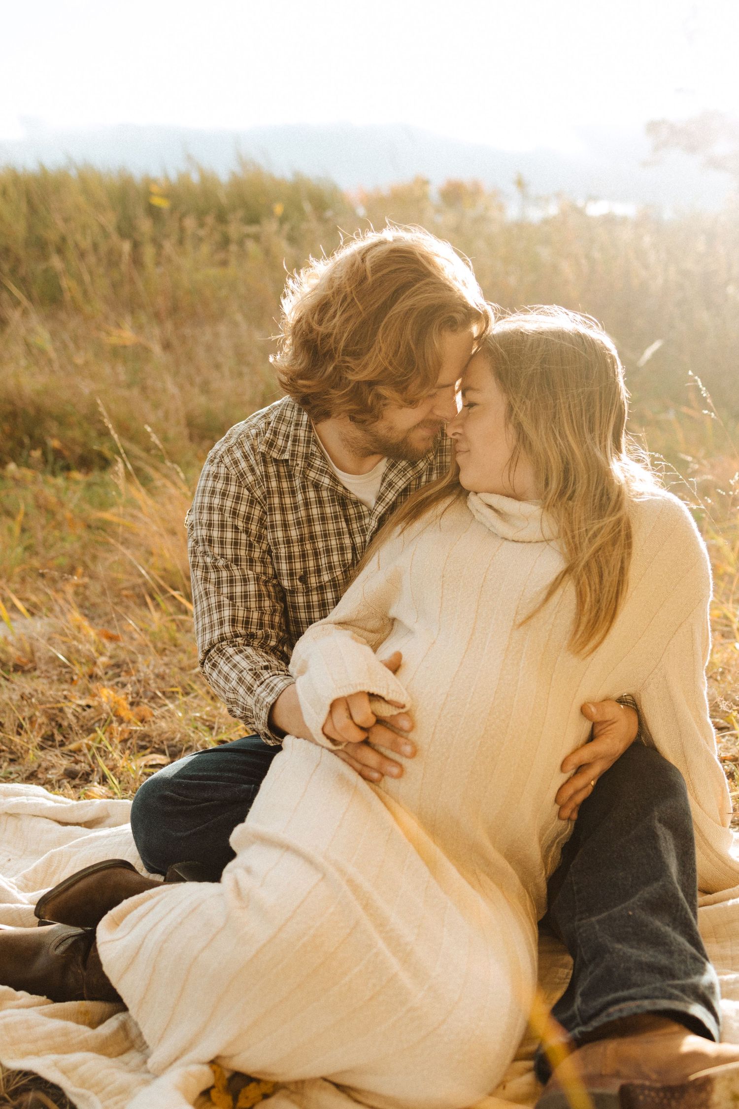 A couple shares an intimate moment while sitting on a blanket in a golden sunlit field during sunset in califon nj.