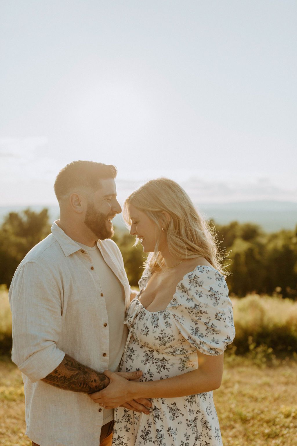 A couple embraces in a sun-drenched field during golden hour with mountains visible in the background in tewksbury nj.