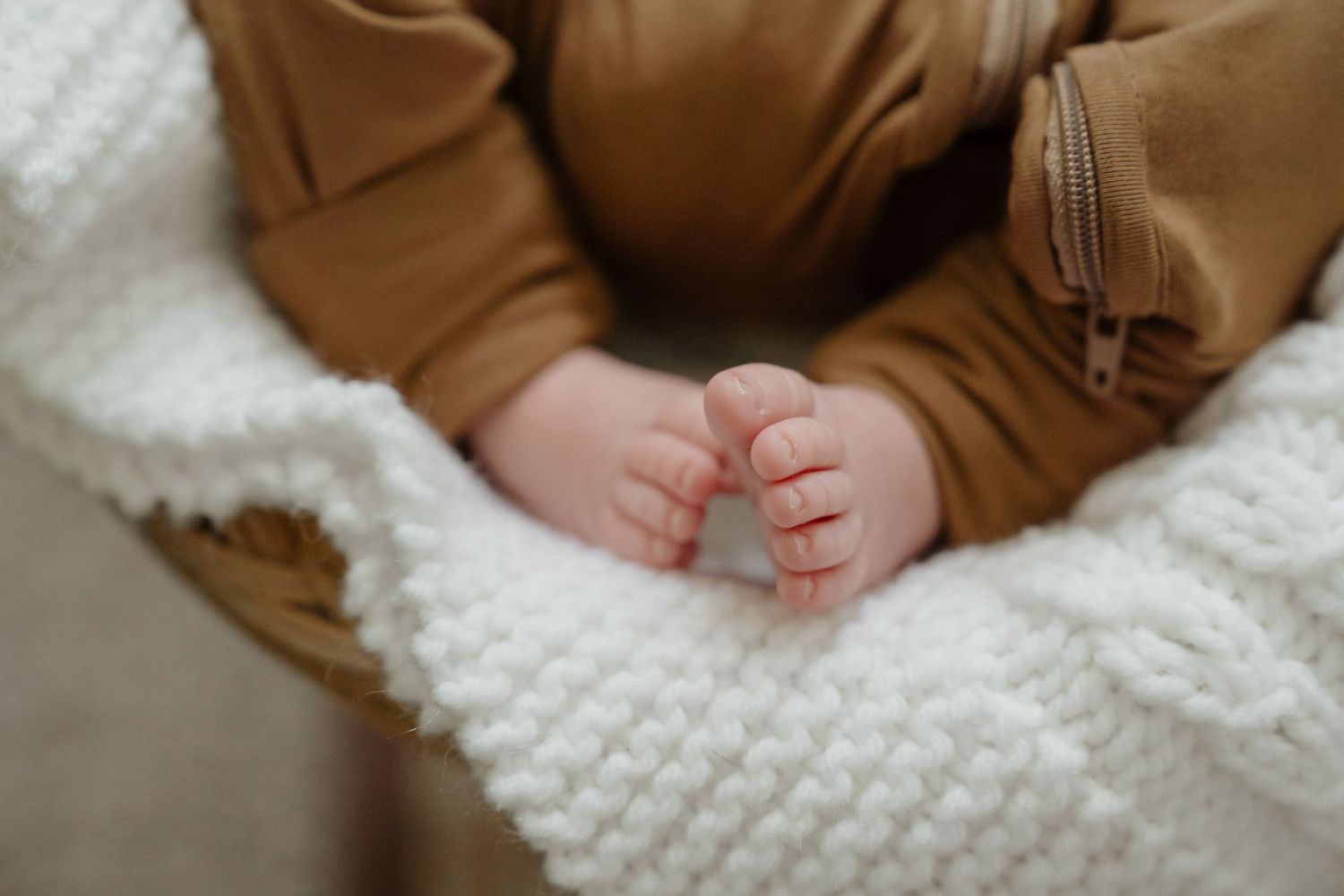 Small baby feet in brown clothing against soft white knitted textile background.
