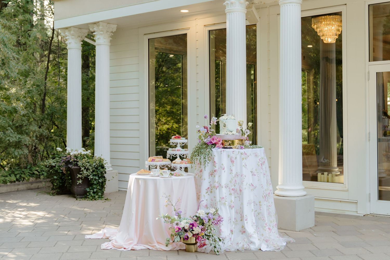 An outdoor wedding reception setup with white lace tablecloths and pink floral arrangements.