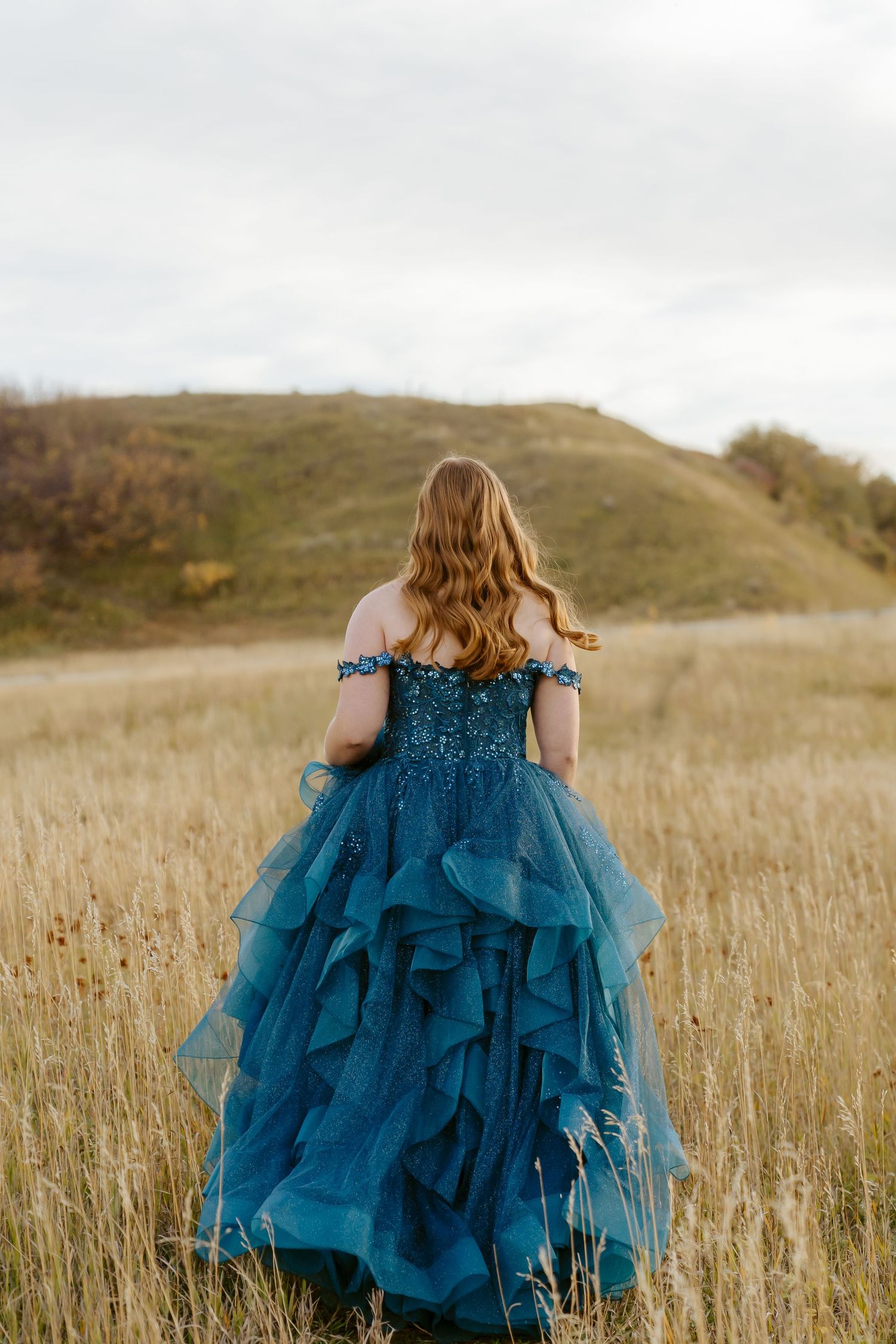 Woman in flowing blue formal gown walking through golden field.
