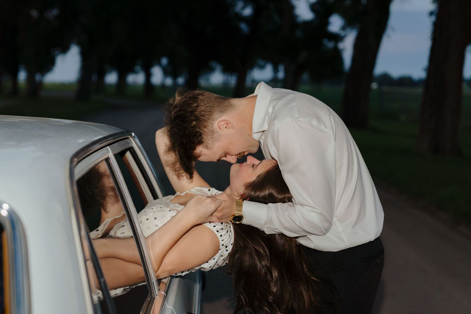 A couple shares a romantic dip and kiss on a tree-lined path during their wedding photoshoot.