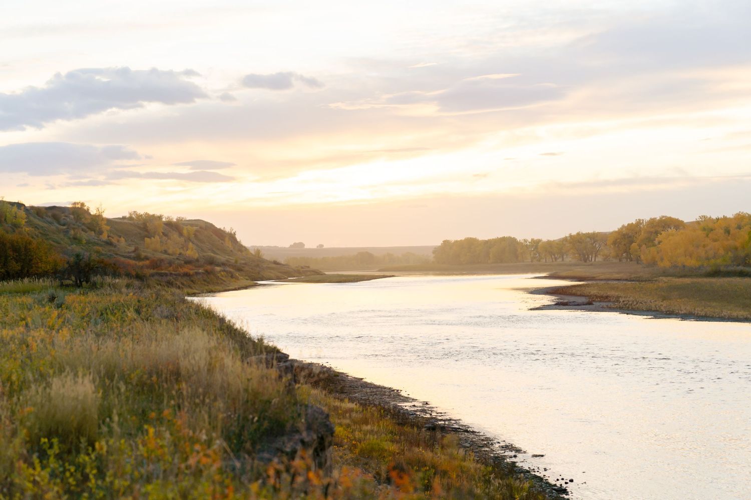 Serene waterway at sunset with golden light illuminating the shoreline and autumn vegetation.