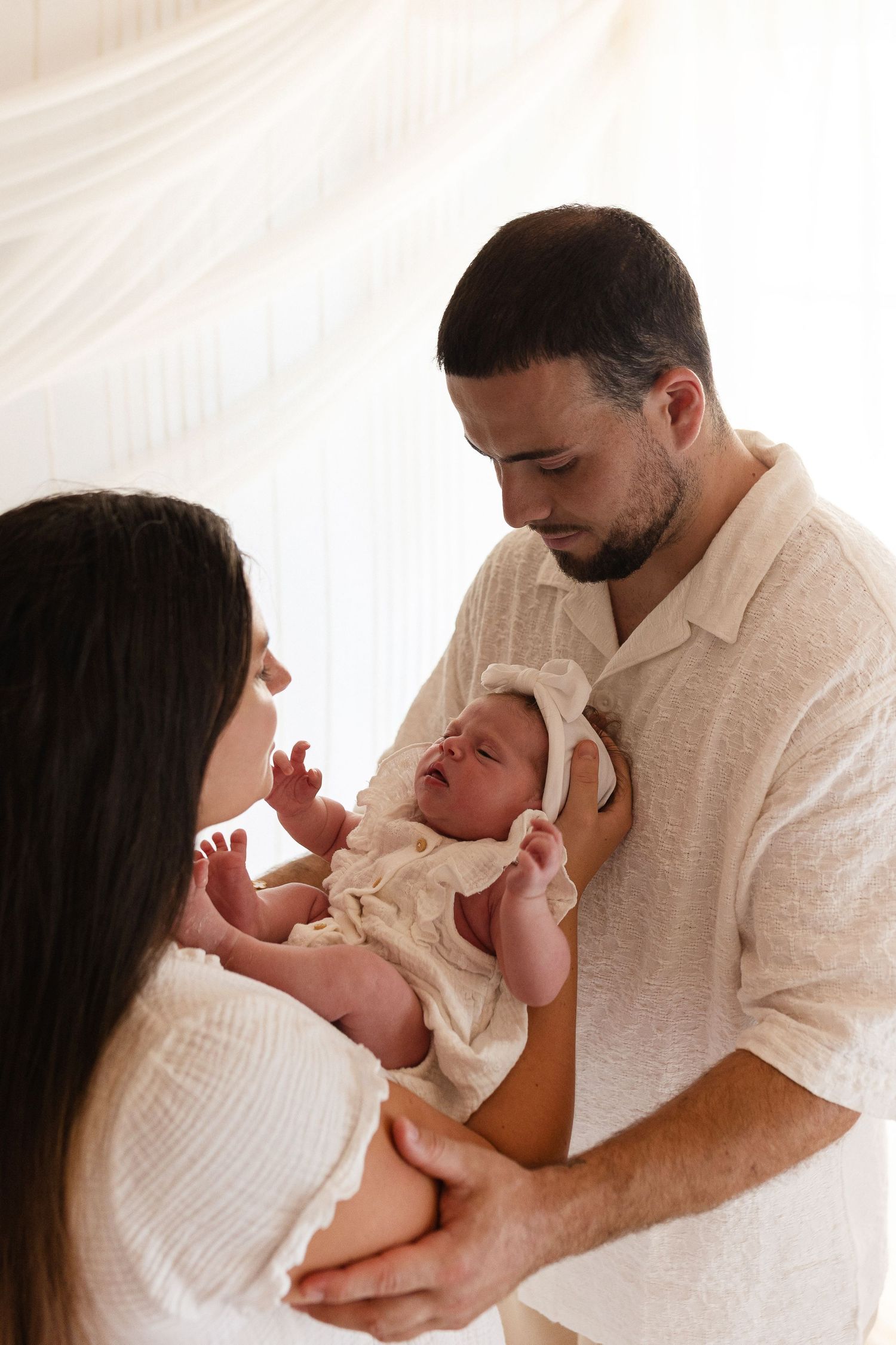 Couple en studio bohème tenant tendrement leur bébé, portrait de famille chaleureux et naturel chez votre photographe à Niort.