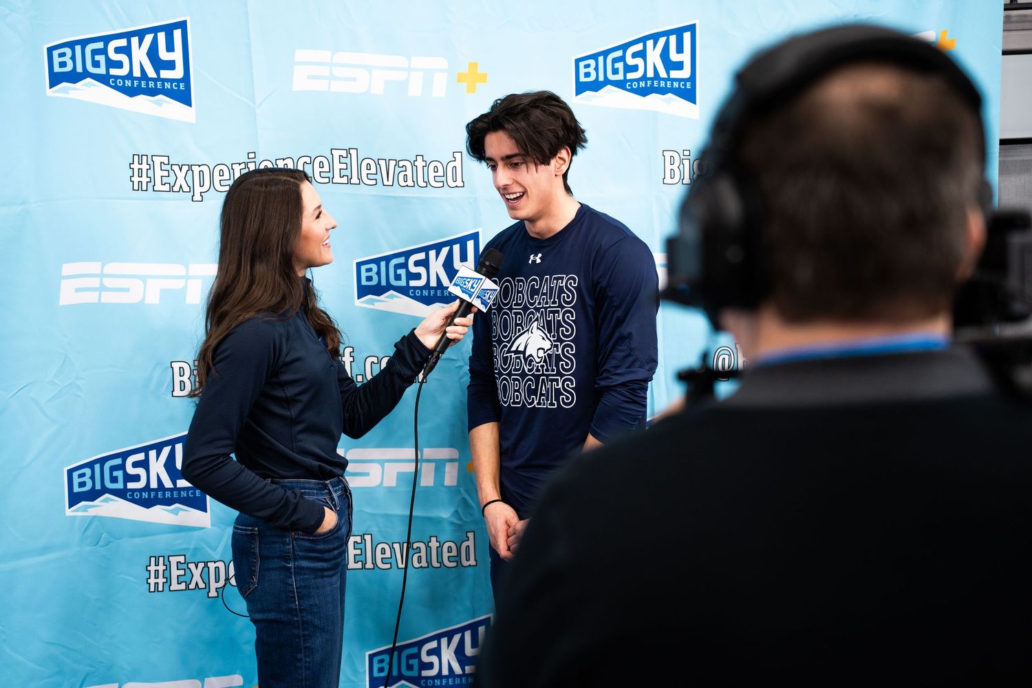 Two people in navy blue shirts interact against a blue backdrop with Big Sky branding.