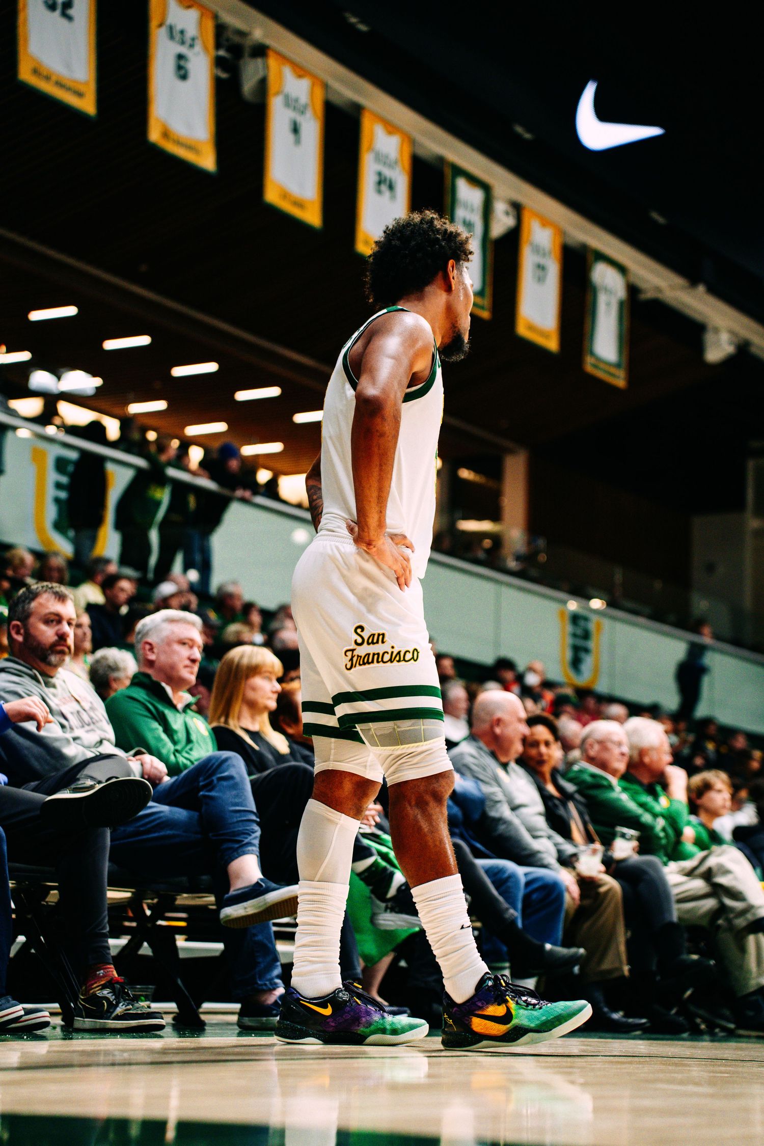 Basketball player wearing Nike shoes and white socks stands on court during game with crowd visible in background.