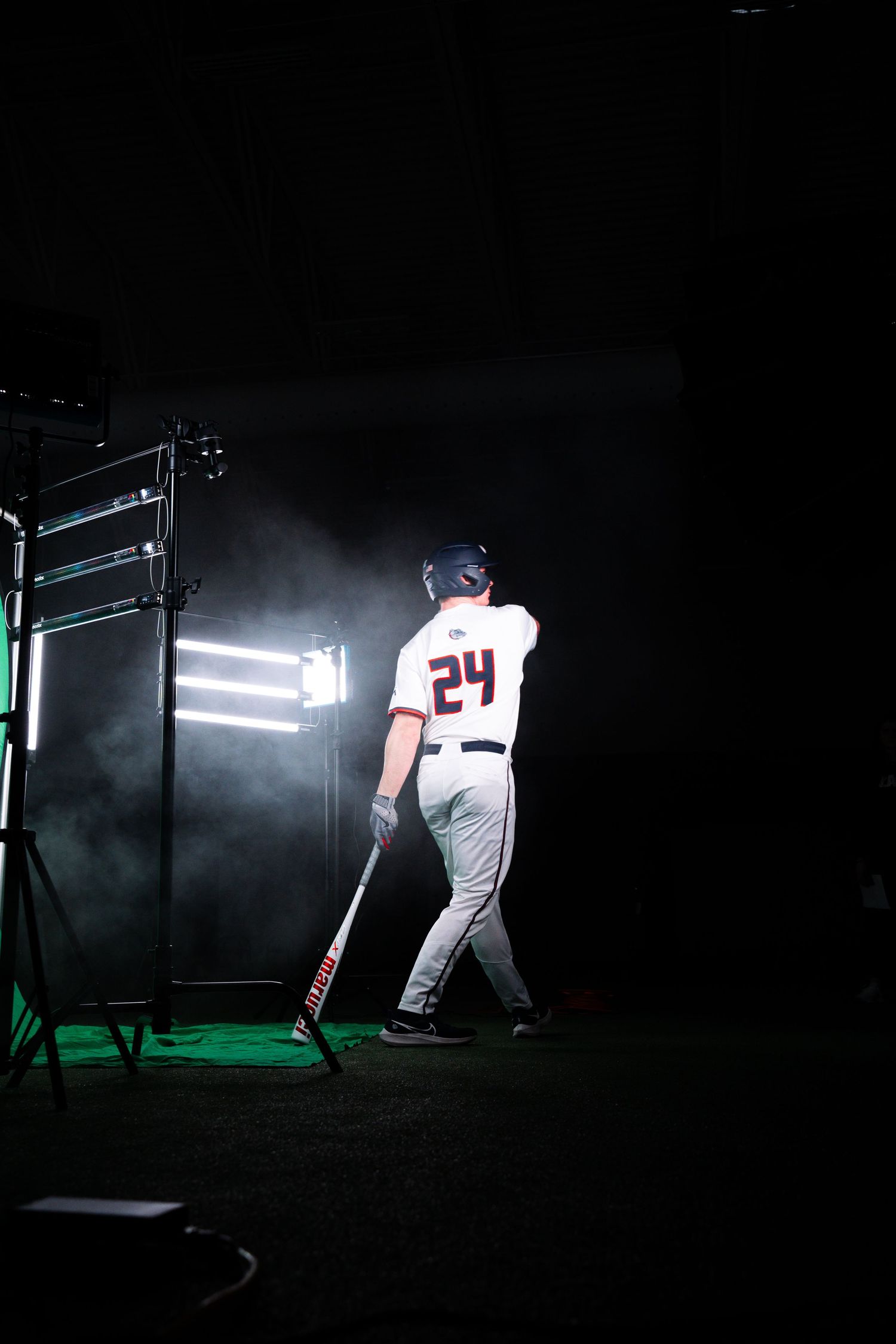 Baseball player in white jersey number 24 walks into dramatic misty lighting during a moody photoshoot.