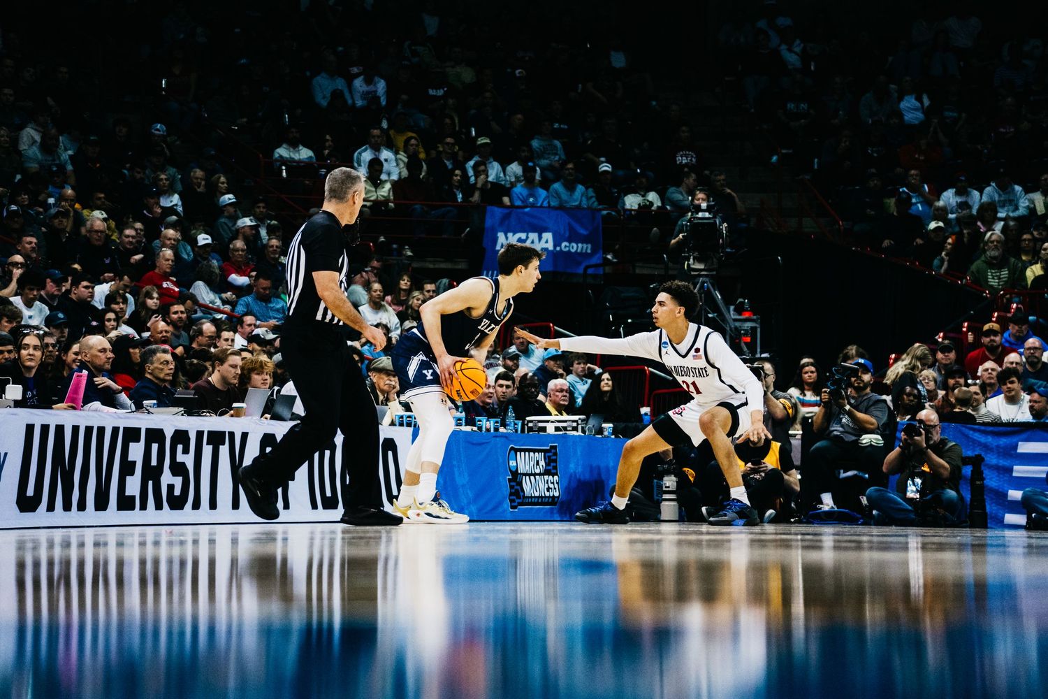 Basketball players leap and stretch across a glossy court floor during an intense NCAA tournament game.