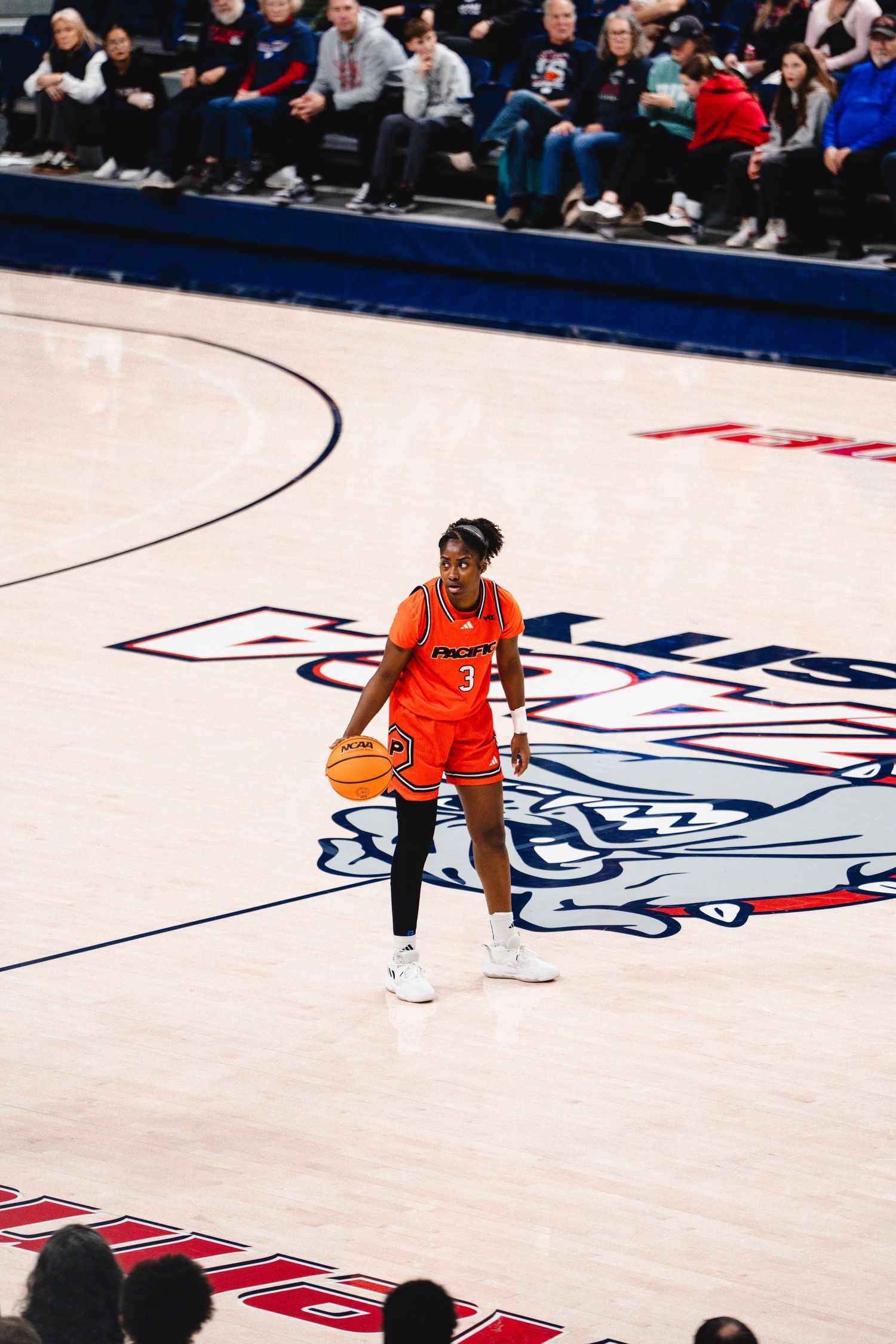 Basketball player in orange uniform dribbling on court with NCAA logo during college game.