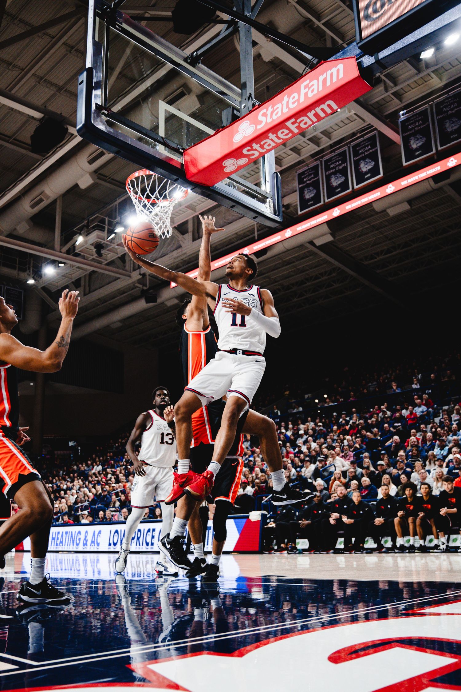 Basketball player makes an athletic layup attempt during a college game as defenders challenge the shot at the rim.