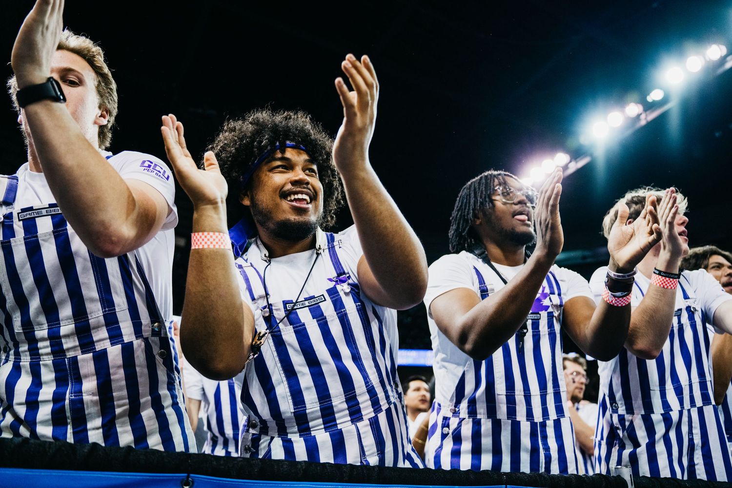Athletes in blue and white striped uniforms clap and cheer enthusiastically on a field at night under bright lights.