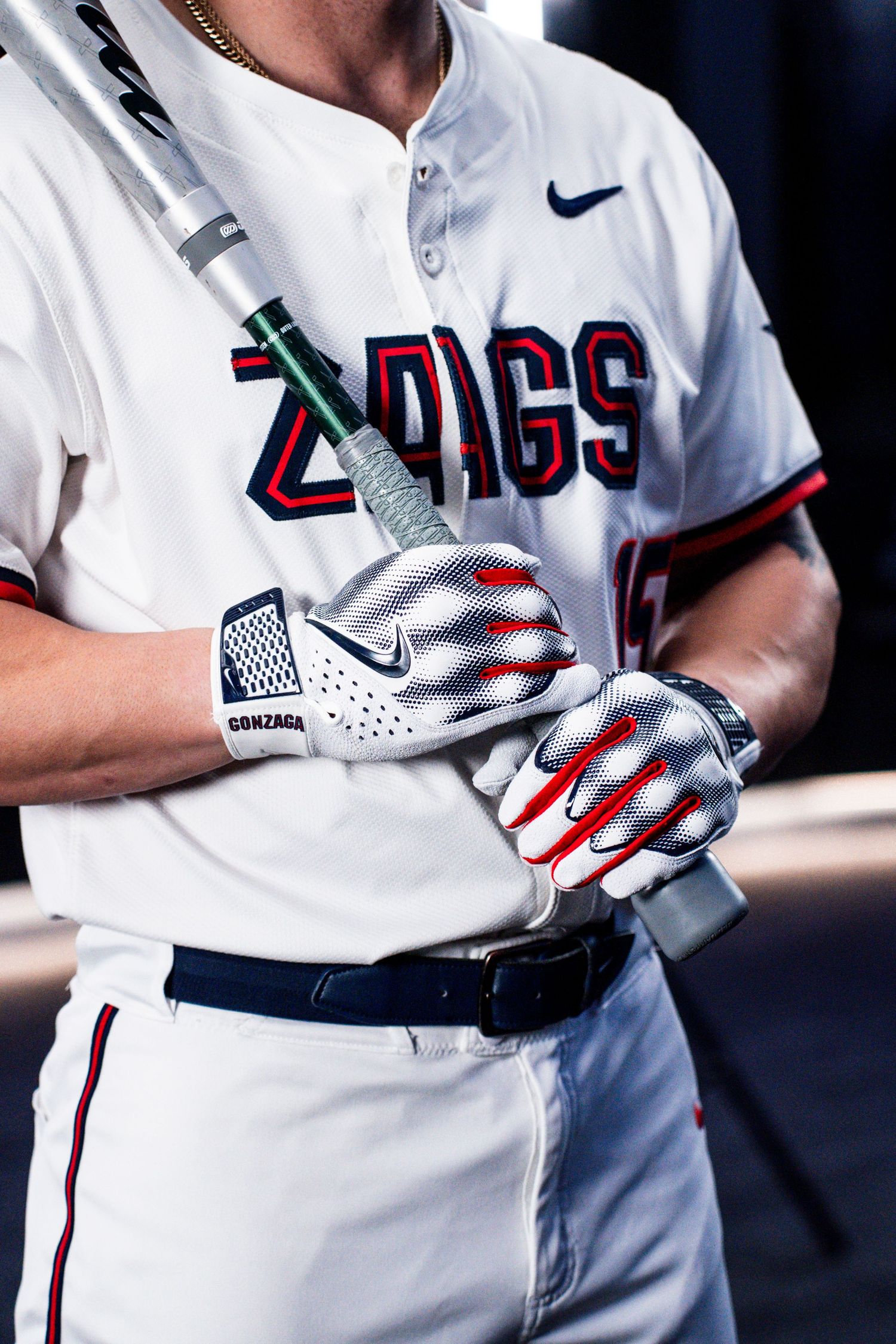 Baseball player in Gonzaga Zags uniform wearing Nike batting gloves holds bat during game.