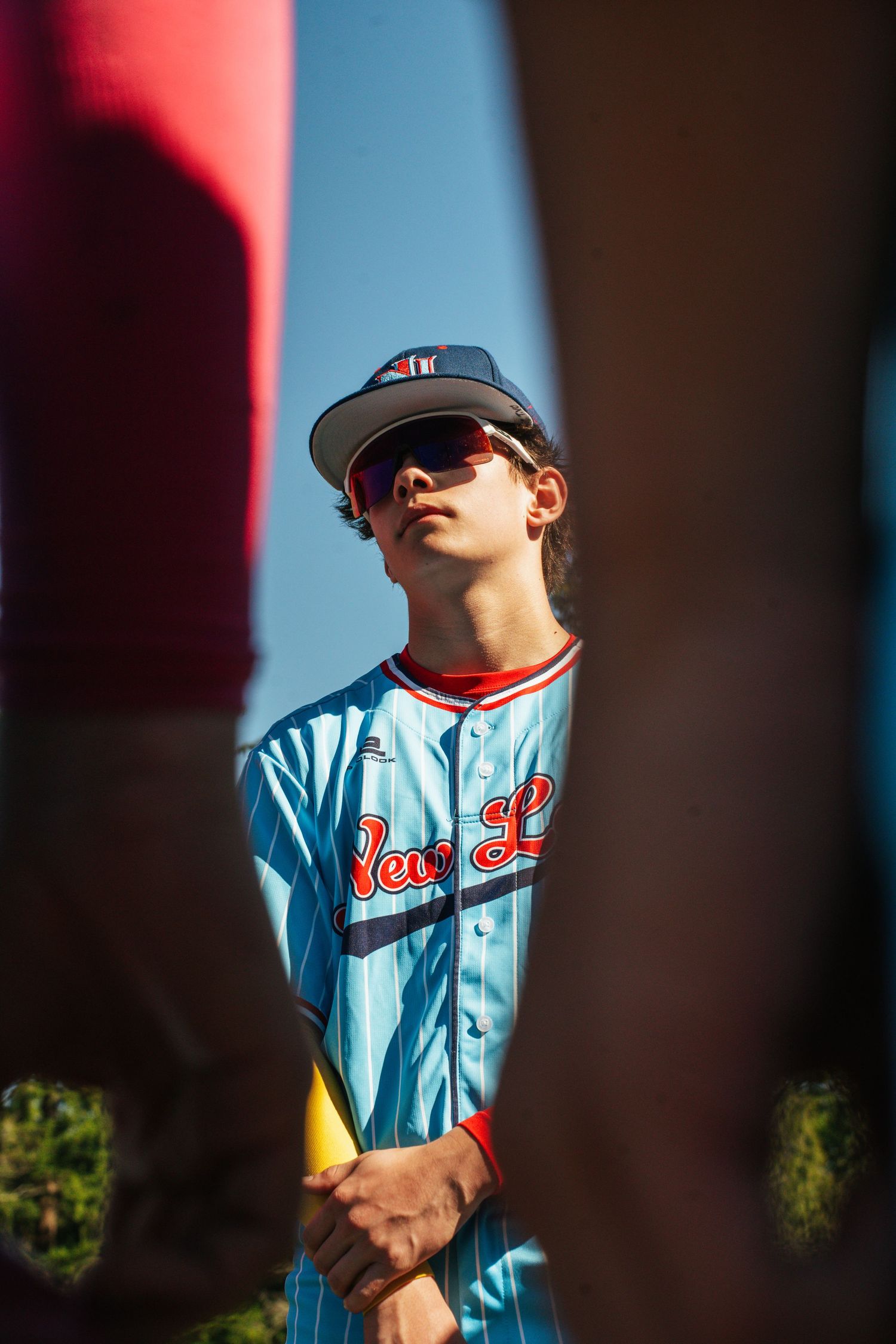 Baseball player wearing light blue jersey and cap stands in dramatic lighting with red and blue shadows.