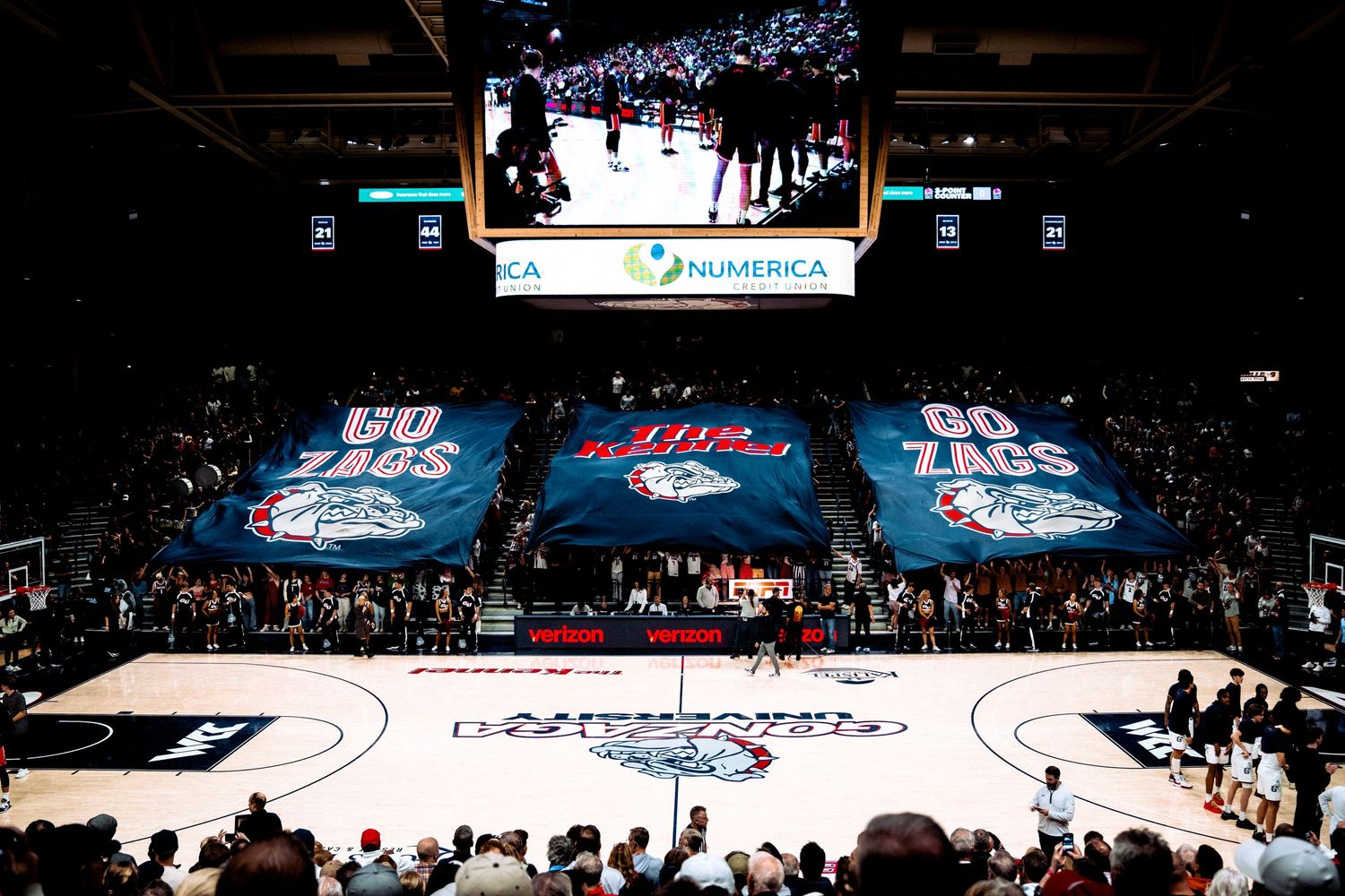 NBA basketball arena with glowing video screens and banners displaying graphics across the court during a game.