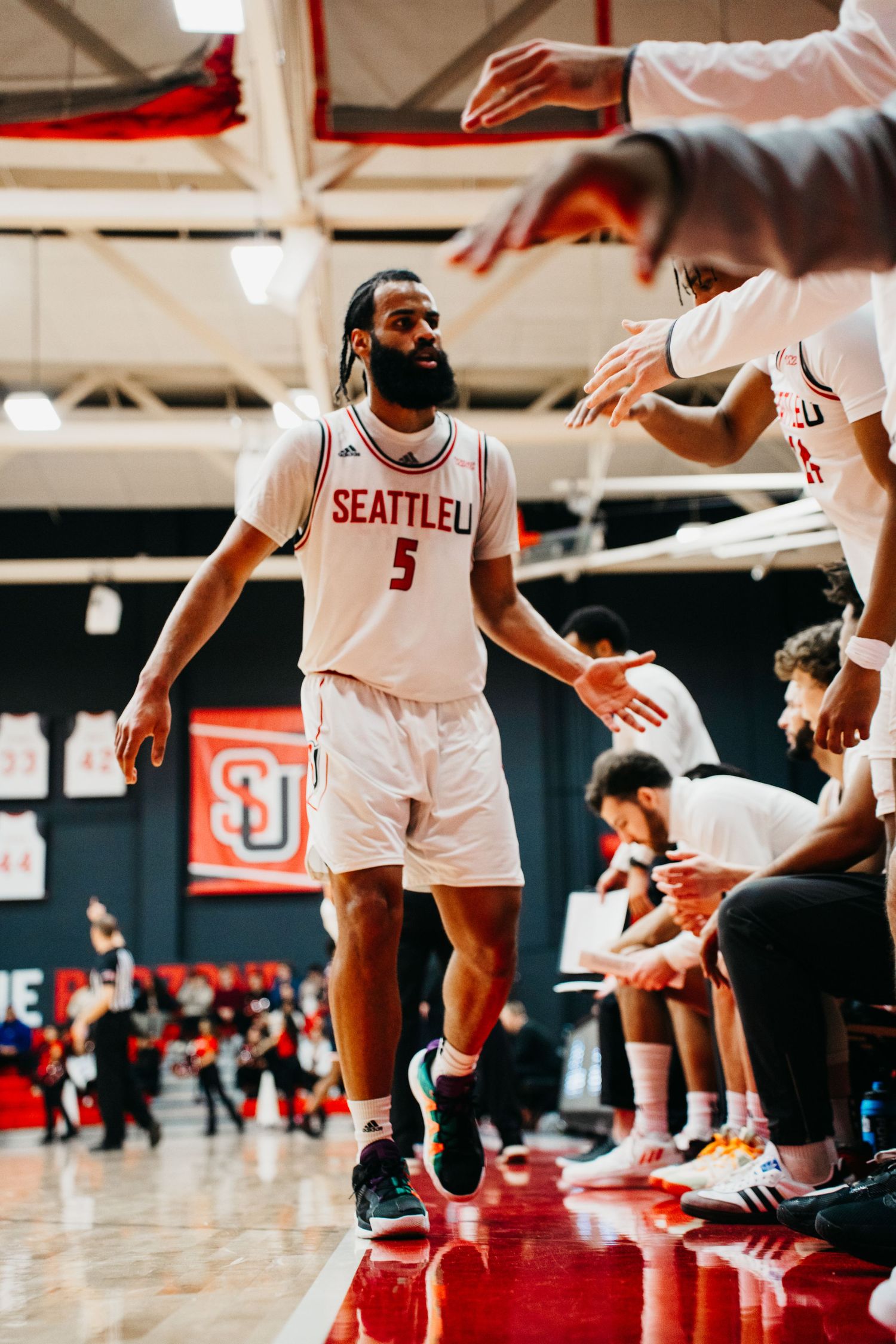 Basketball player in Seattle U jersey high-fives teammates on sideline during game.