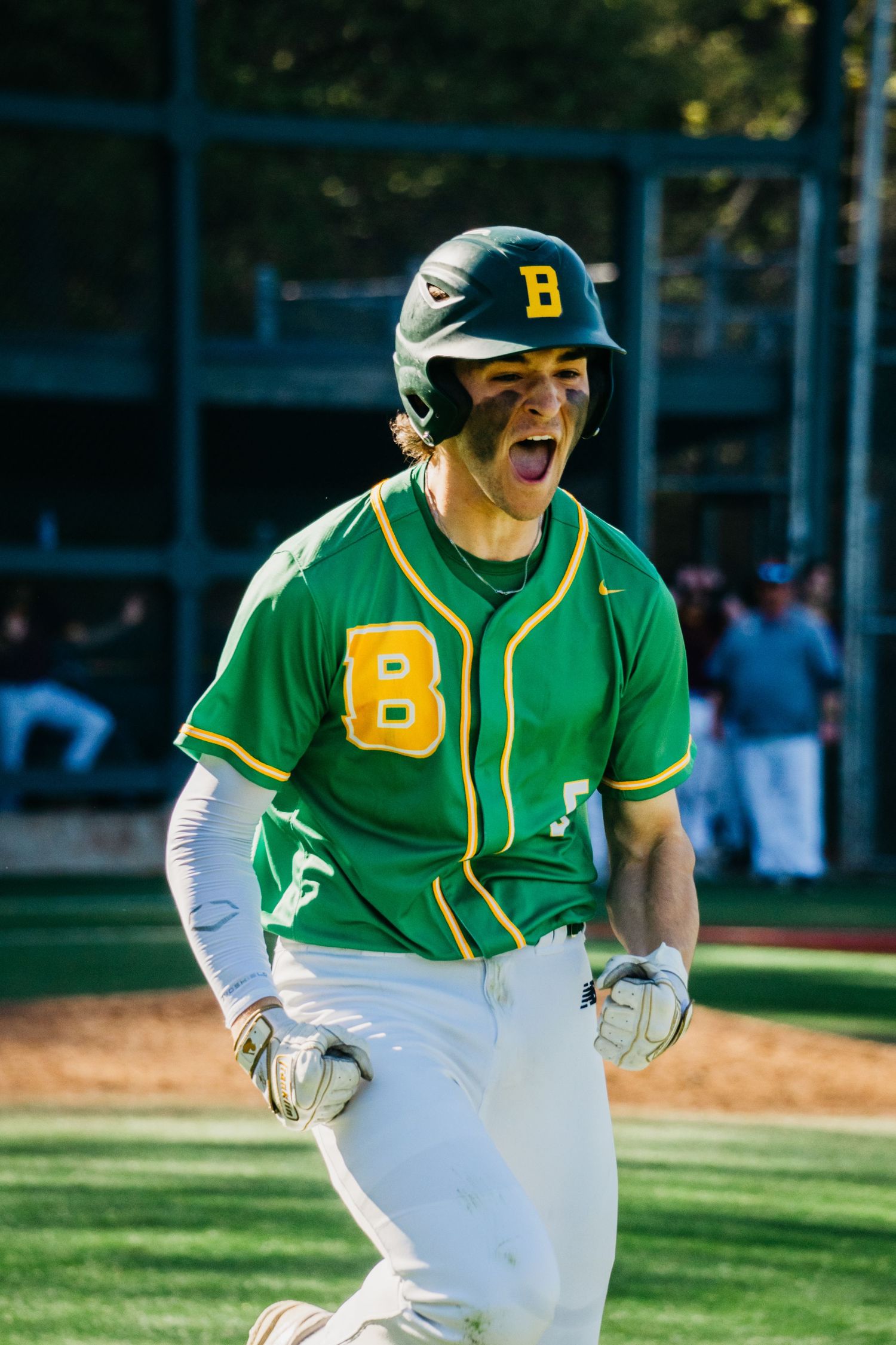 Baseball player in green and white uniform running on field during game shows intense expression of effort.