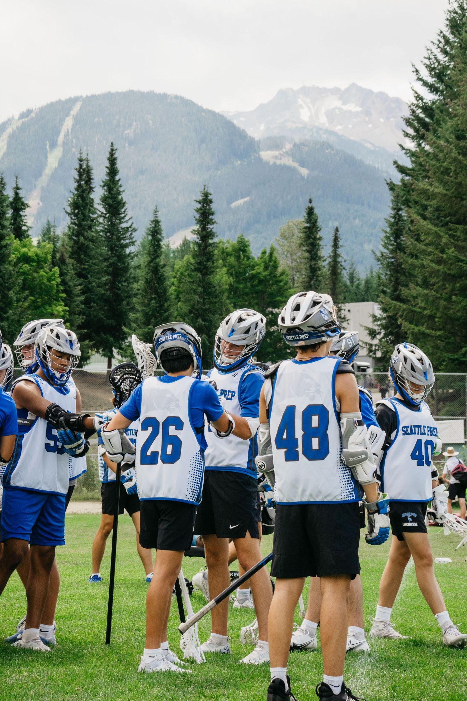 Women's lacrosse team lined up on a grass field with mountain views and evergreen trees in the background.