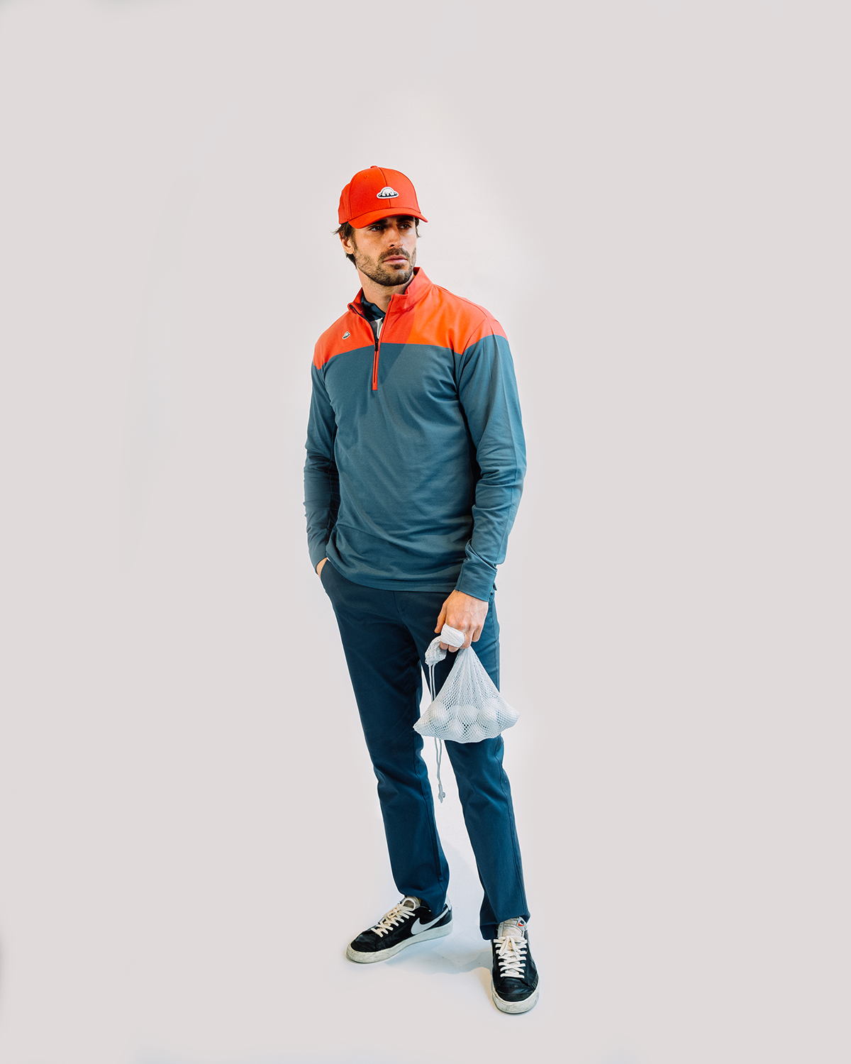 Person in teal and orange color-blocked quarter-zip pullover and navy pants poses against light background.