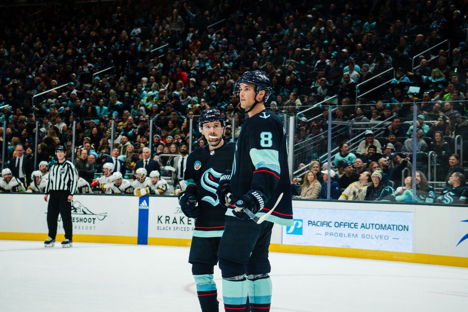 A Seattle Kraken hockey player in the team's teal and navy uniform stands on the ice during a home game at Climate Pledge Arena.