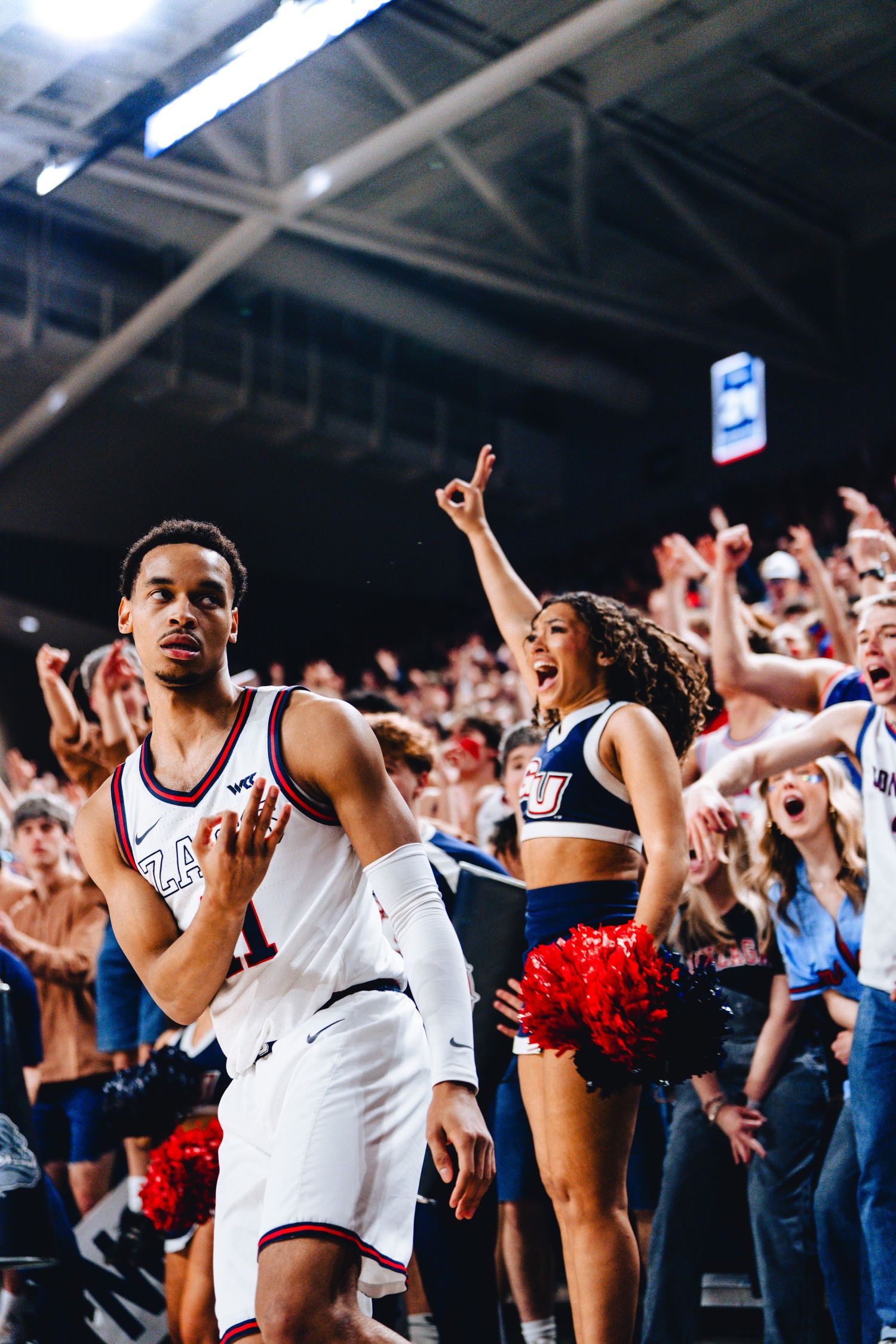 Basketball player celebrates with cheerleader and crowd during exciting college basketball game moment.