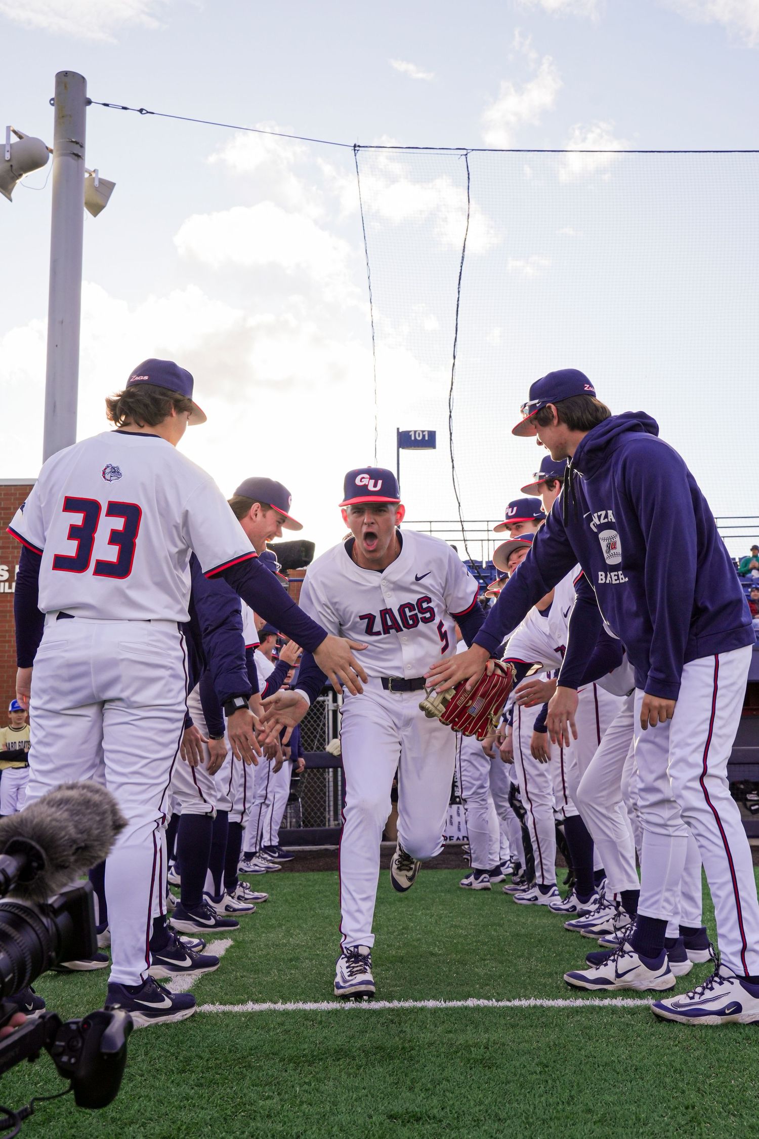 Baseball players in white and navy uniforms line up for introductions before a game on a turf field.