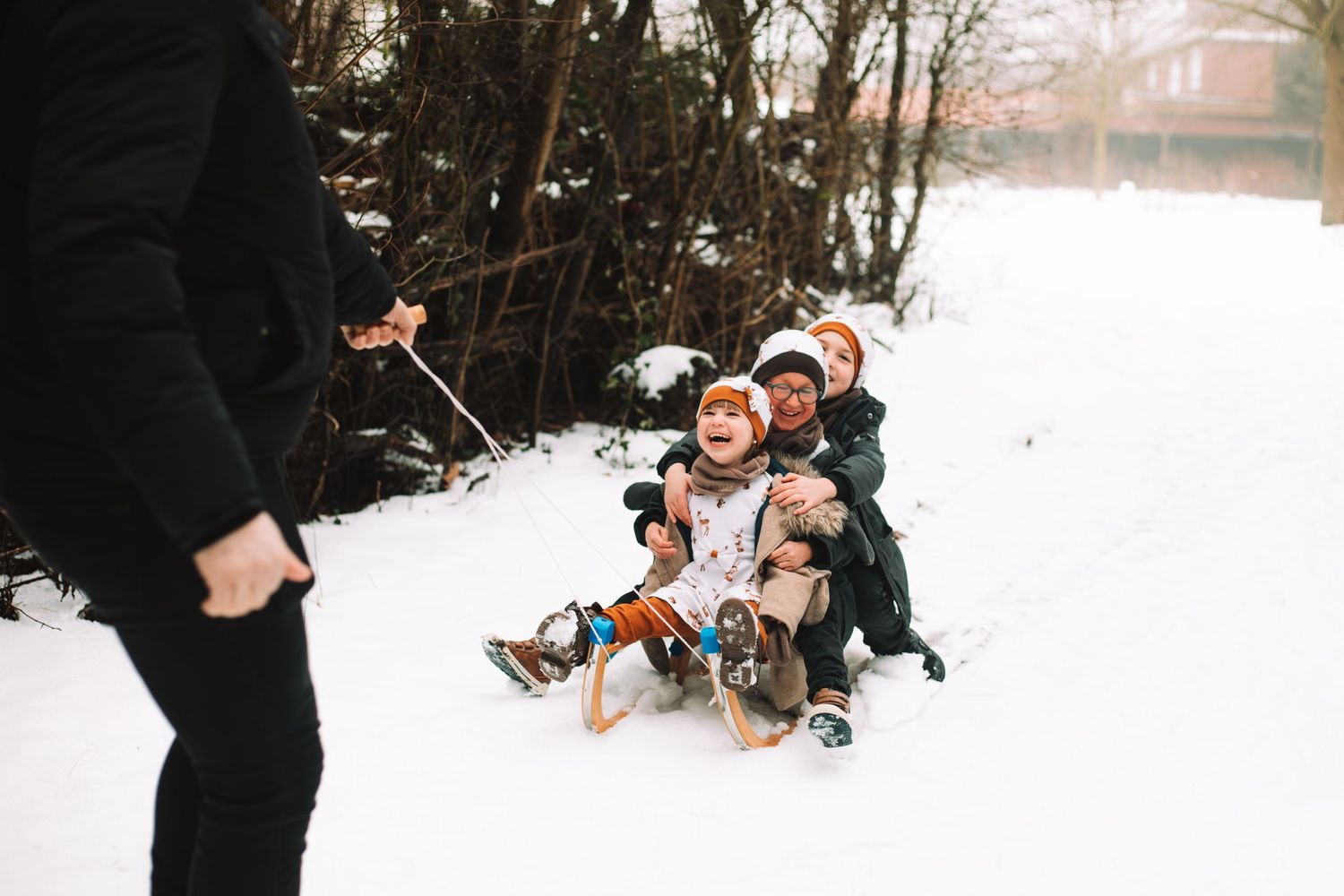 Gezinsshoot in de sneeuw. Kinderen die op een slee zitten die voortgetrokken wordt door één van de ouders.