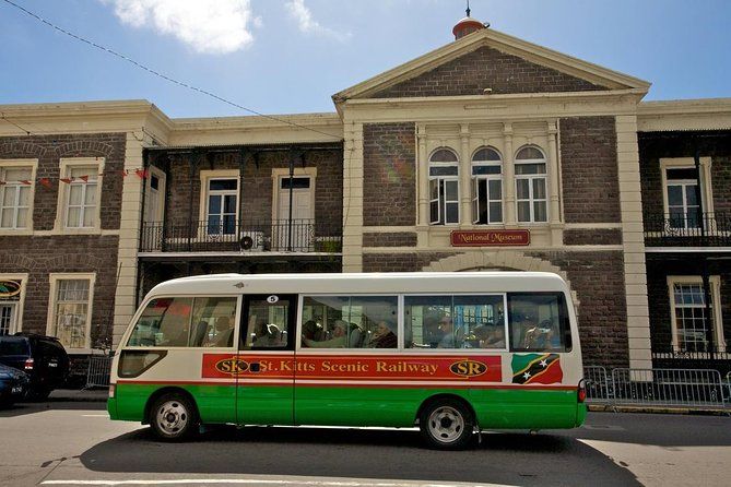 St. Kitts Scenic Railway green and red bus parked in front of a historic colonial building in Basseterre.
