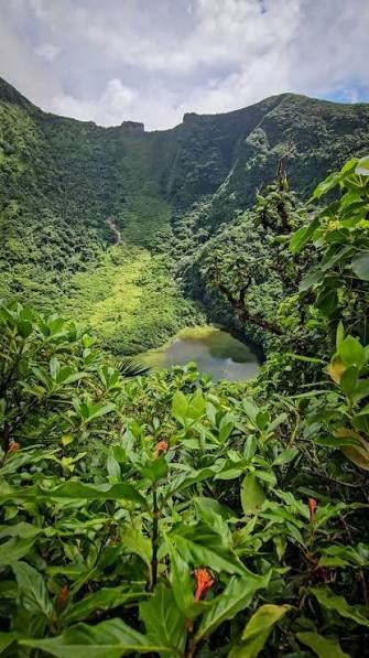 Lush green volcanic crater with a hidden lake surrounded by tropical rainforest vegetation and misty mountain peaks.